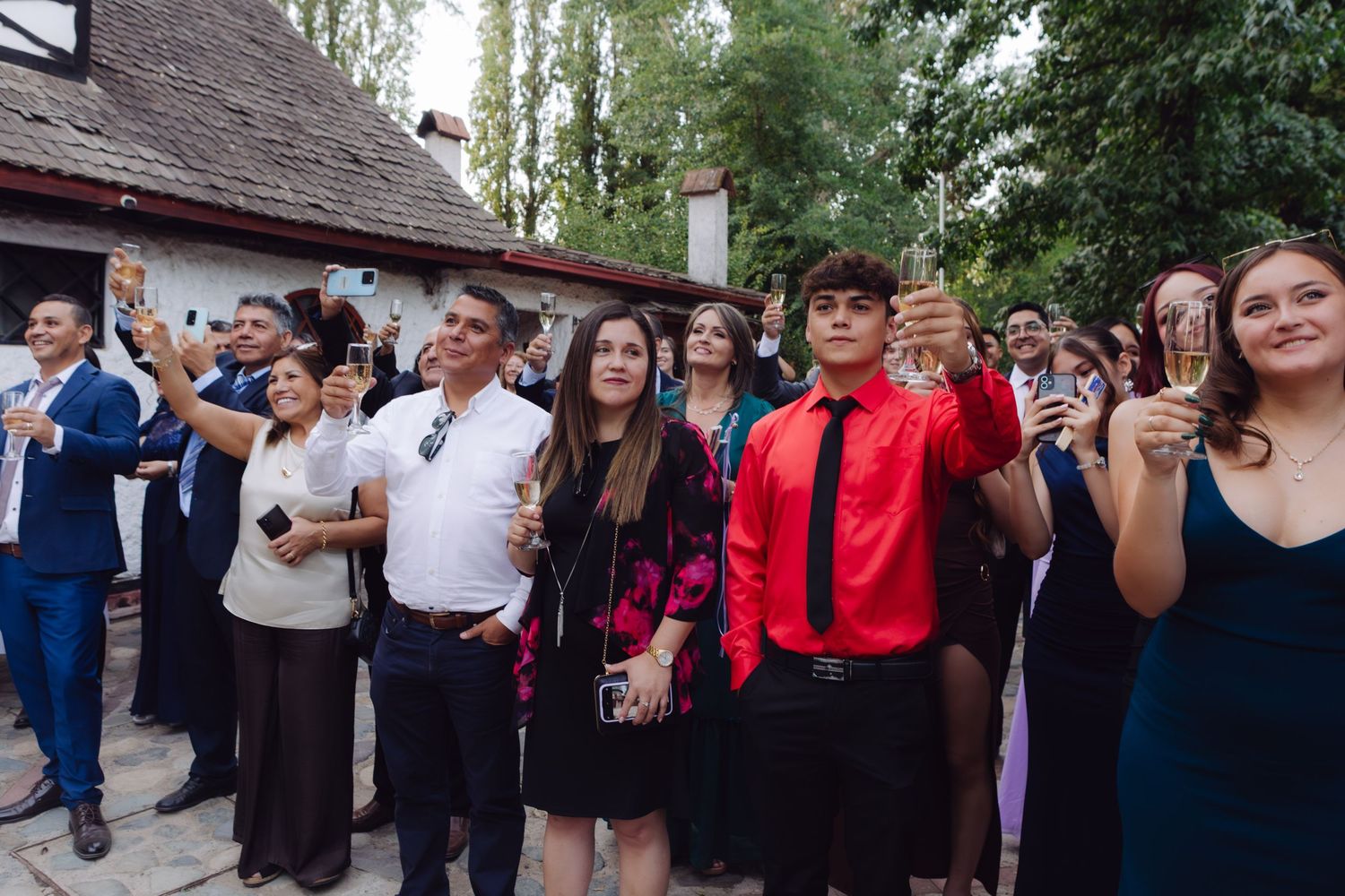 Wedding guests raise champagne glasses in celebratory toast outside rustic stone venue building.