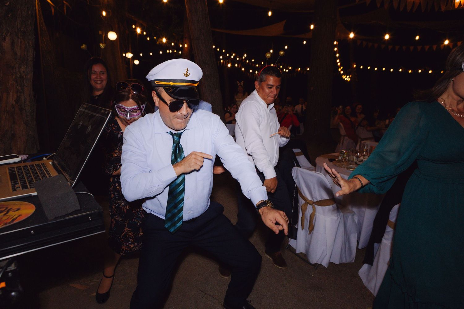 Guest in captain hat and sunglasses dancing energetically at wedding reception.