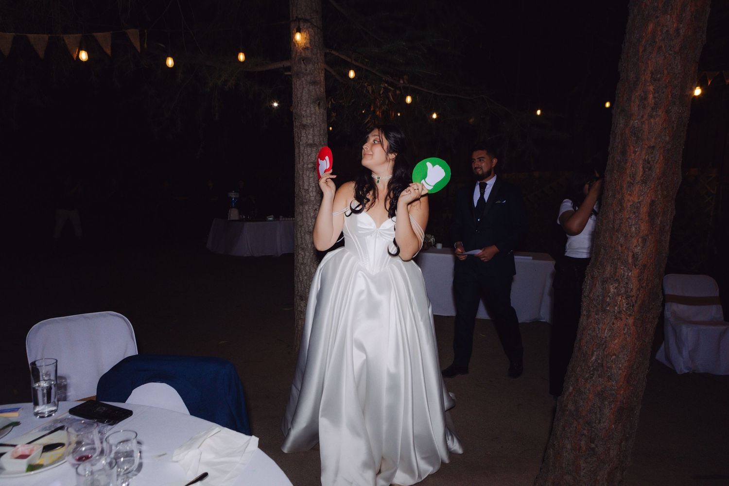 Bride in white gown juggling colorful balloons at outdoor wedding reception.