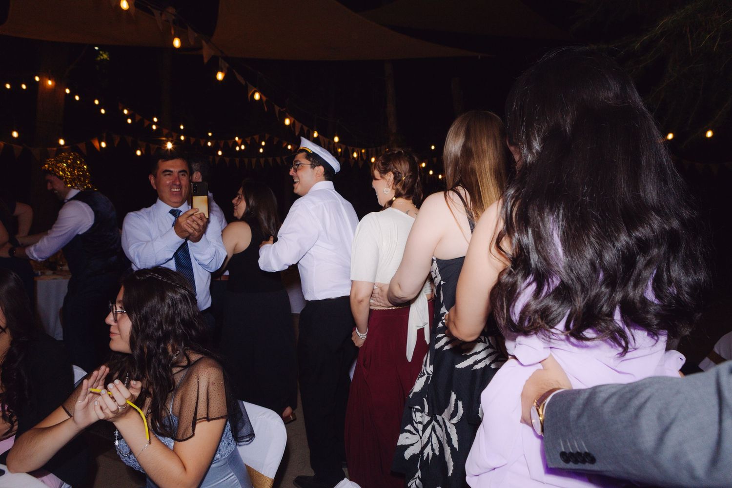 Guests dancing and celebrating at an outdoor wedding reception with string lights overhead.