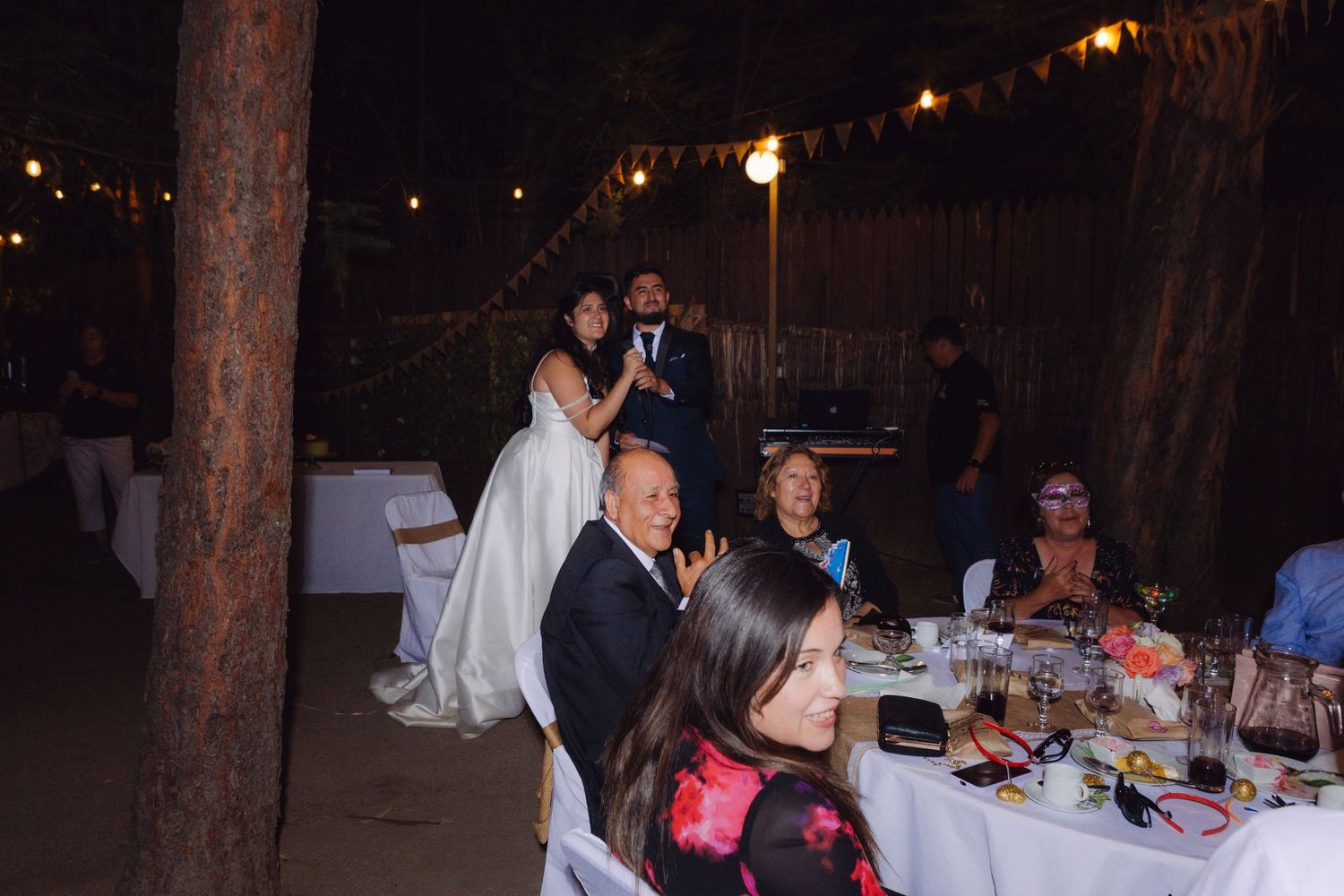 Bride in white gown poses with guests at an elegant outdoor wedding reception dinner.