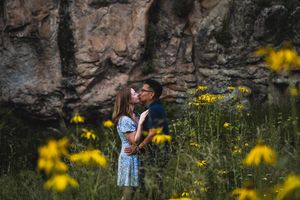 Couple sharing a romantic moment among yellow wildflowers with rocky cliffs in the background.