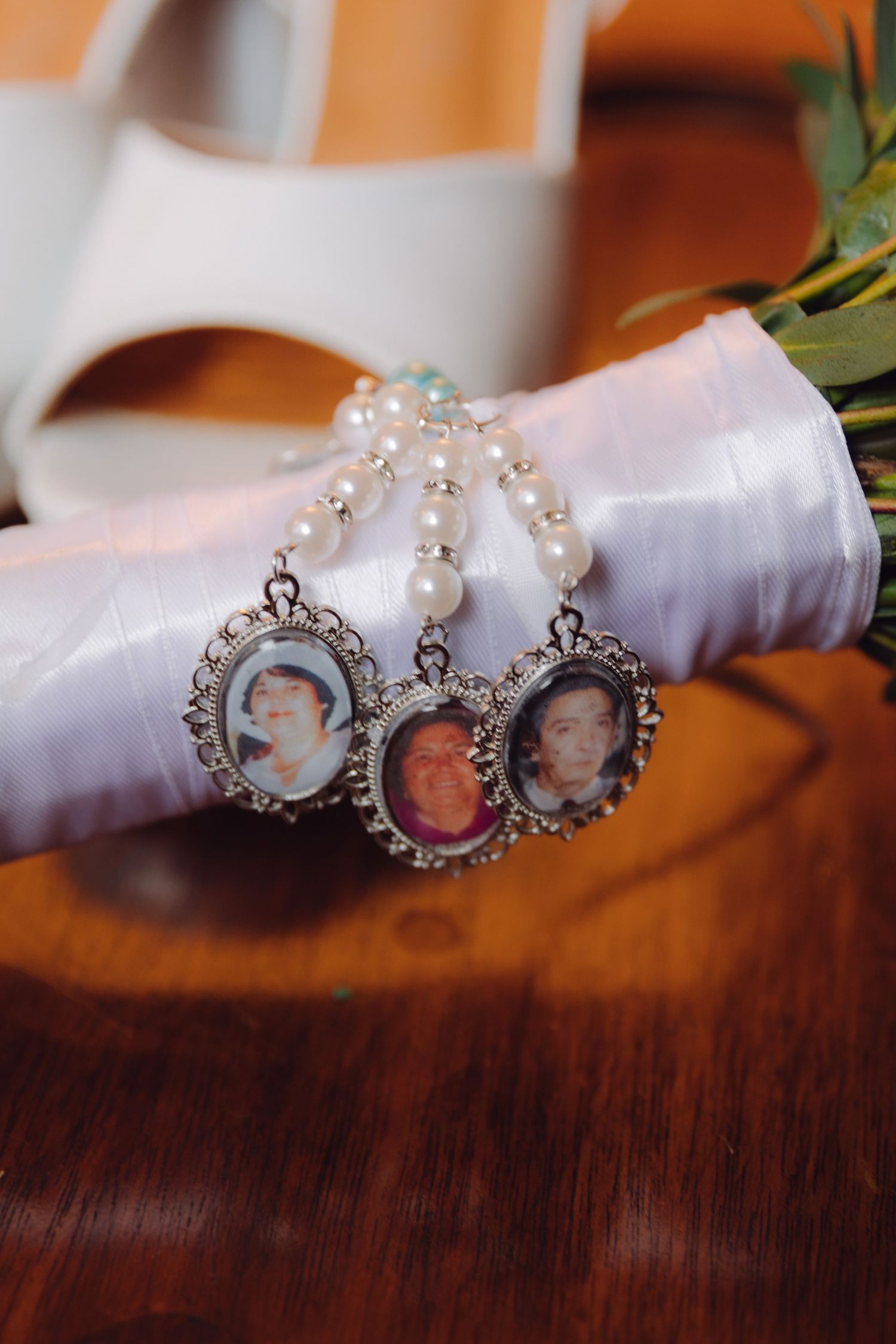 Three vintage oval photo memorial charms on a pearl bracelet resting against white bridal heels.