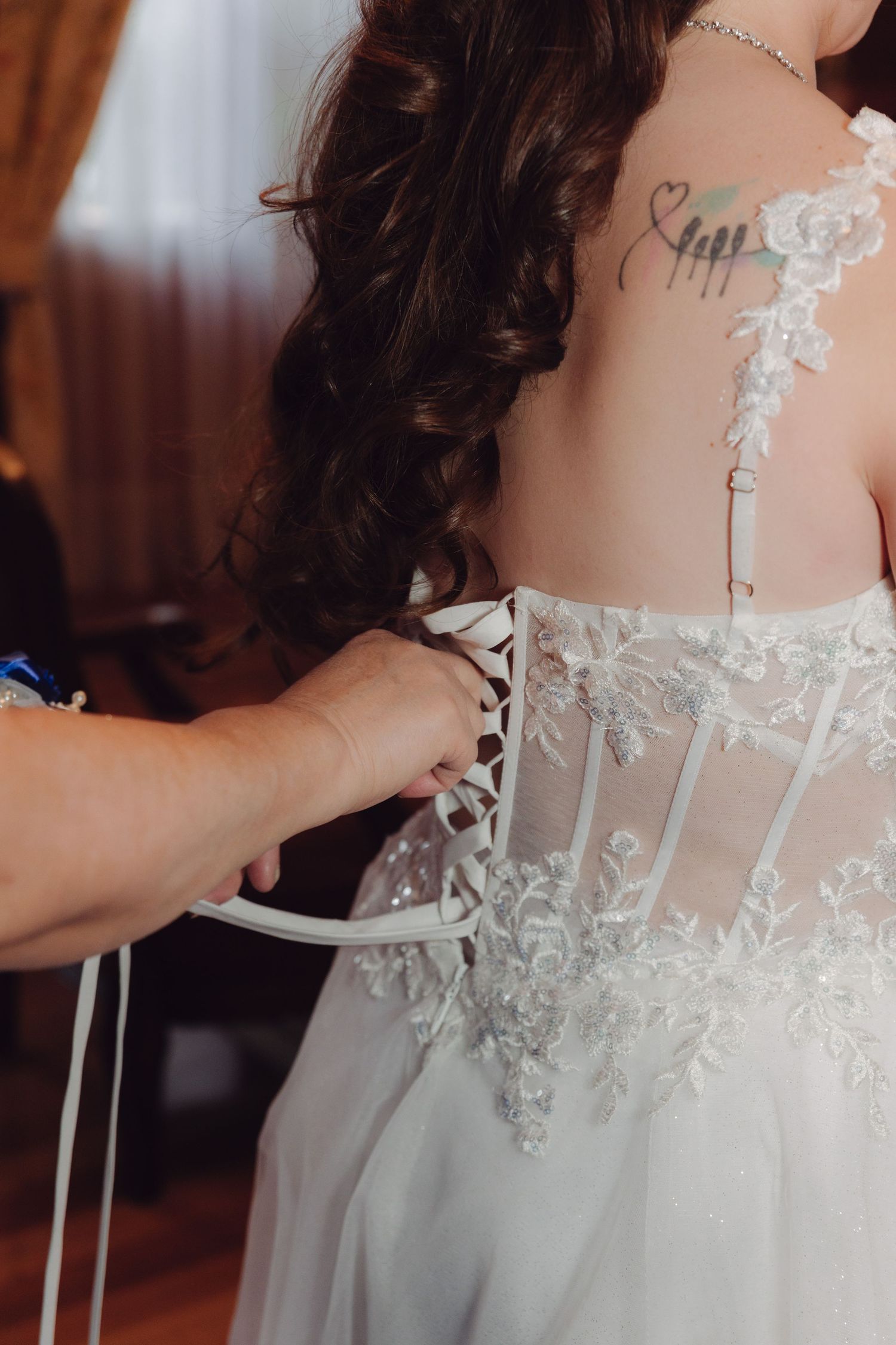 Close-up of a wedding dress being laced up on a bride with a heart tattoo on her upper back.