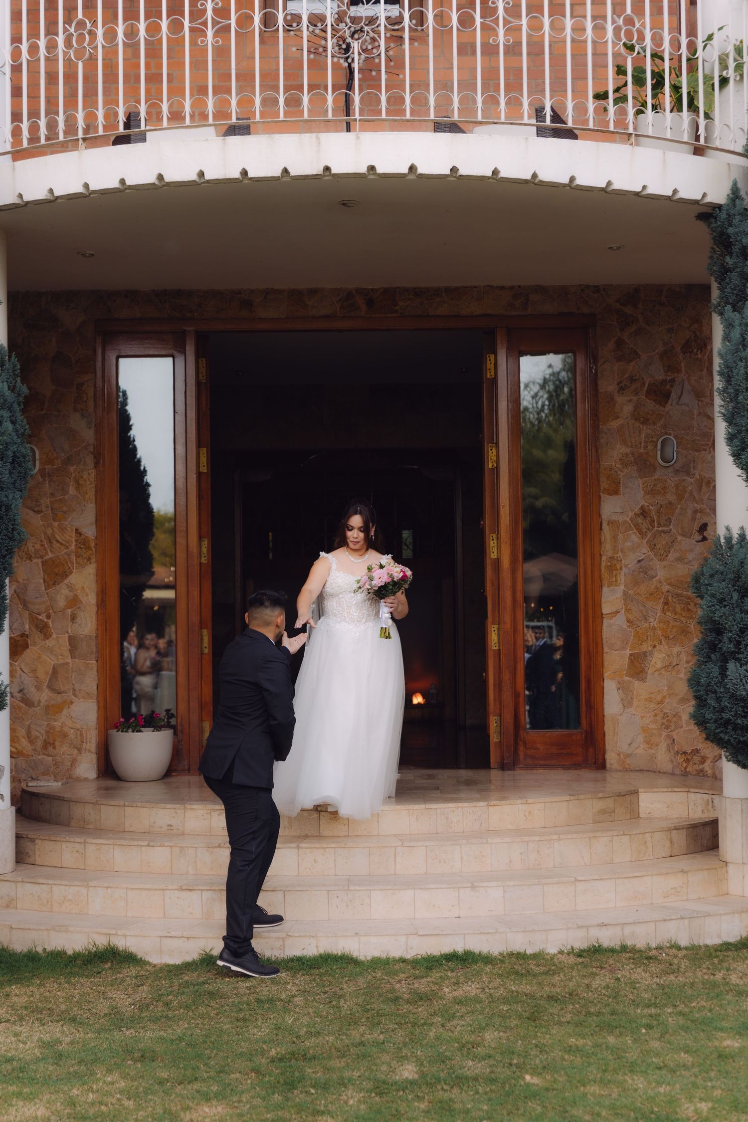 Groom reaching up to assist bride in white gown descending steps of stone wedding venue.