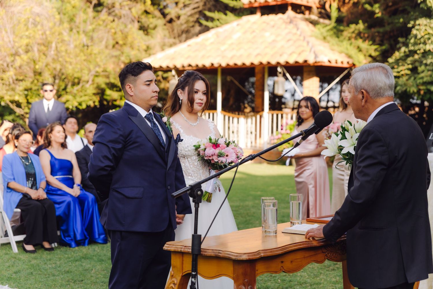 Bride and groom exchanging vows at outdoor wedding ceremony before officiant at microphone.
