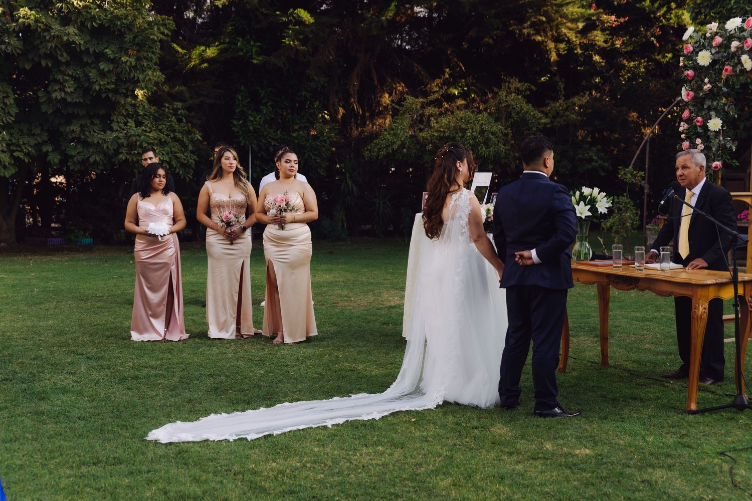 Bride and groom exchange vows at an outdoor garden wedding ceremony with bridesmaids in pink dresses.
