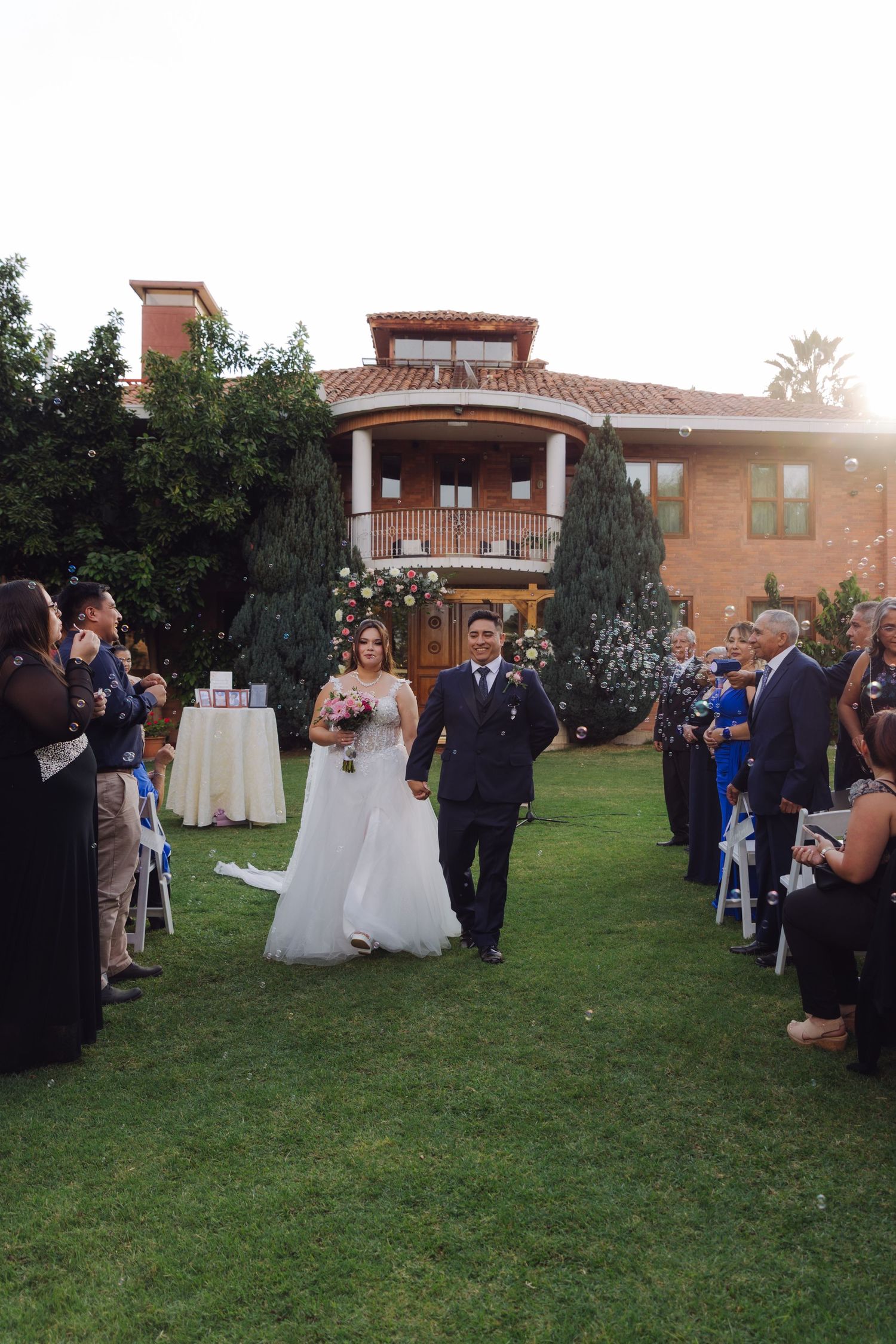Newlywed couple walks back down the aisle as guests celebrate at elegant outdoor garden wedding ceremony.