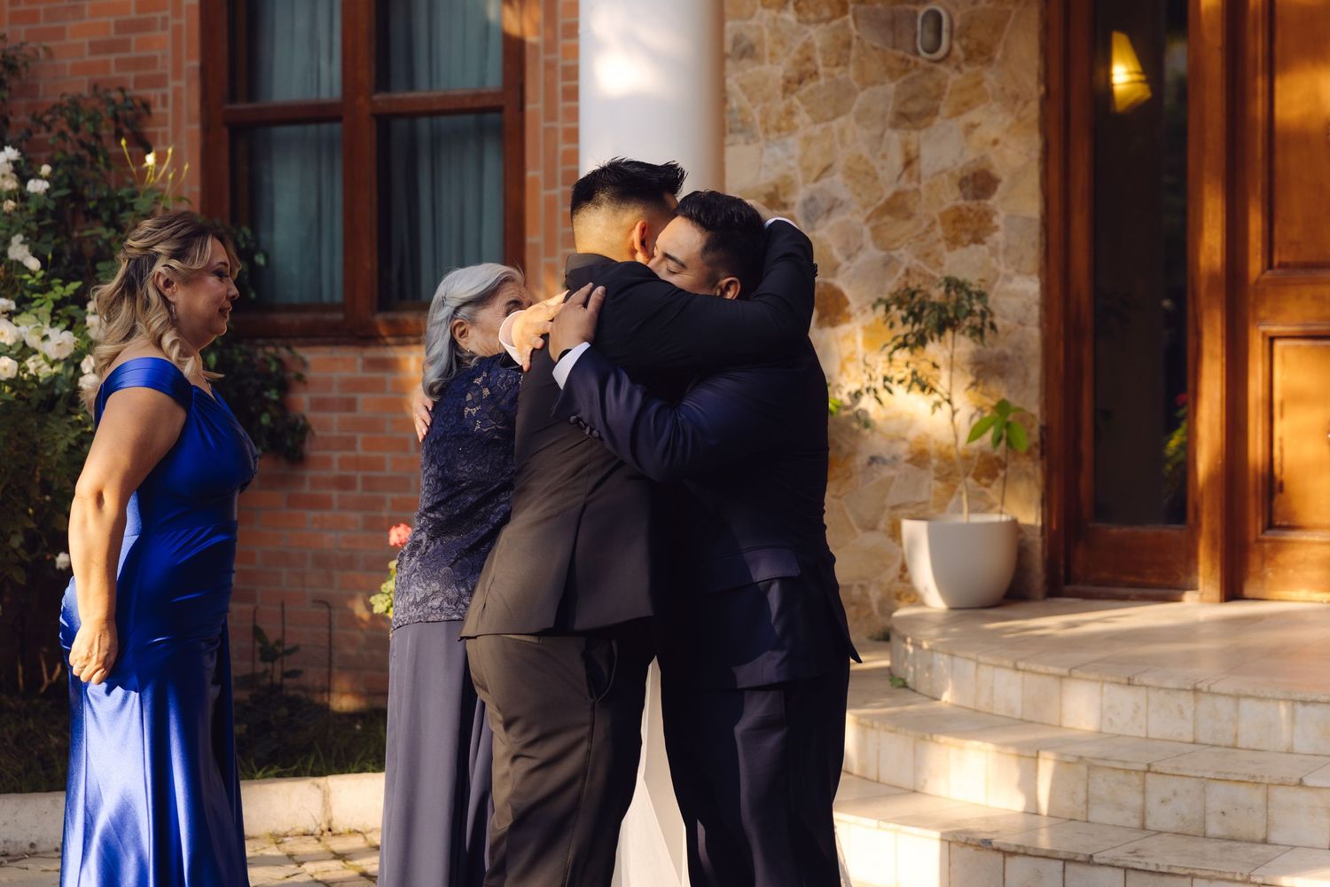 Emotional group hug between groom and family members outside illuminated stone venue after wedding ceremony.