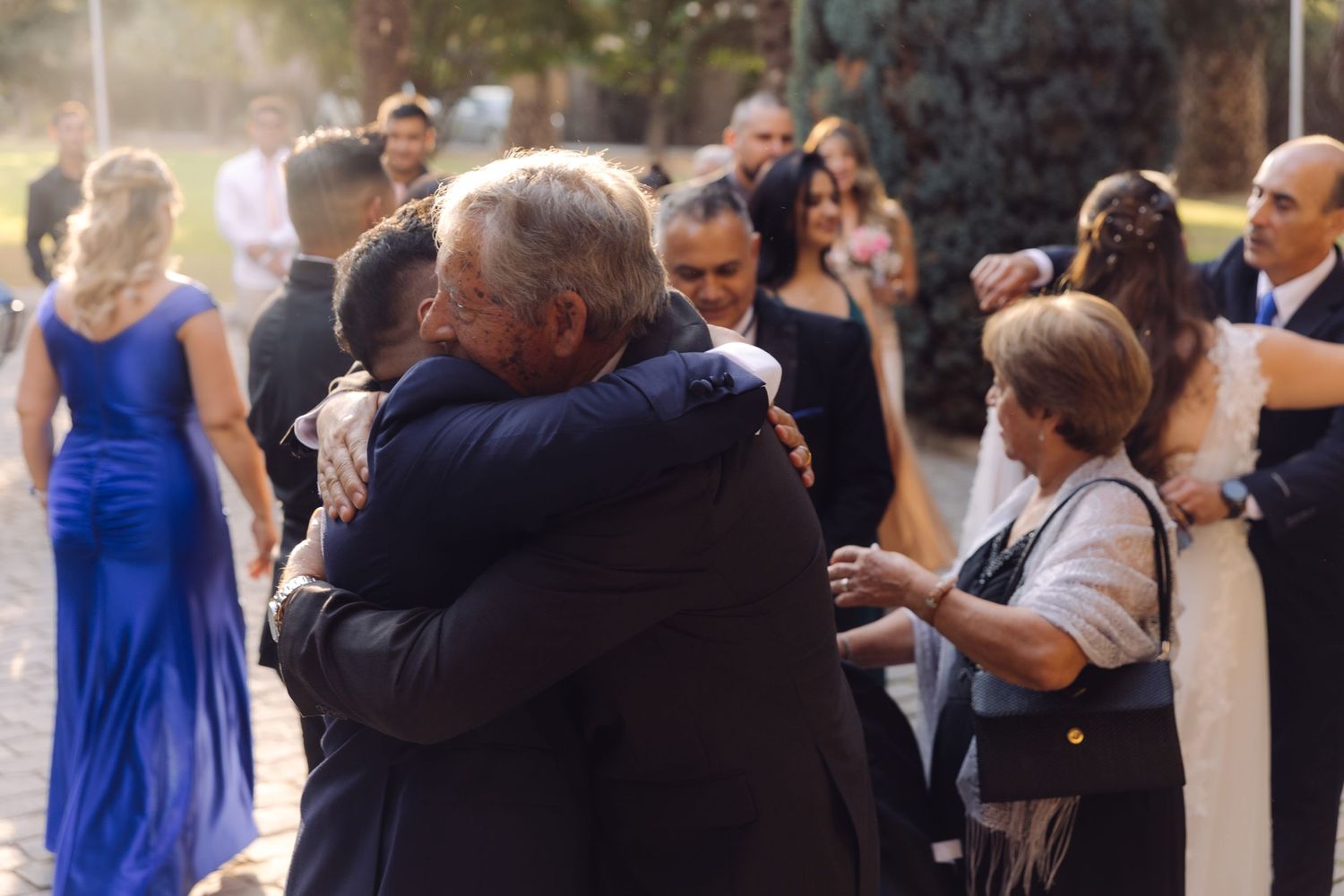 Guests embracing and hugging at an outdoor wedding reception celebration.