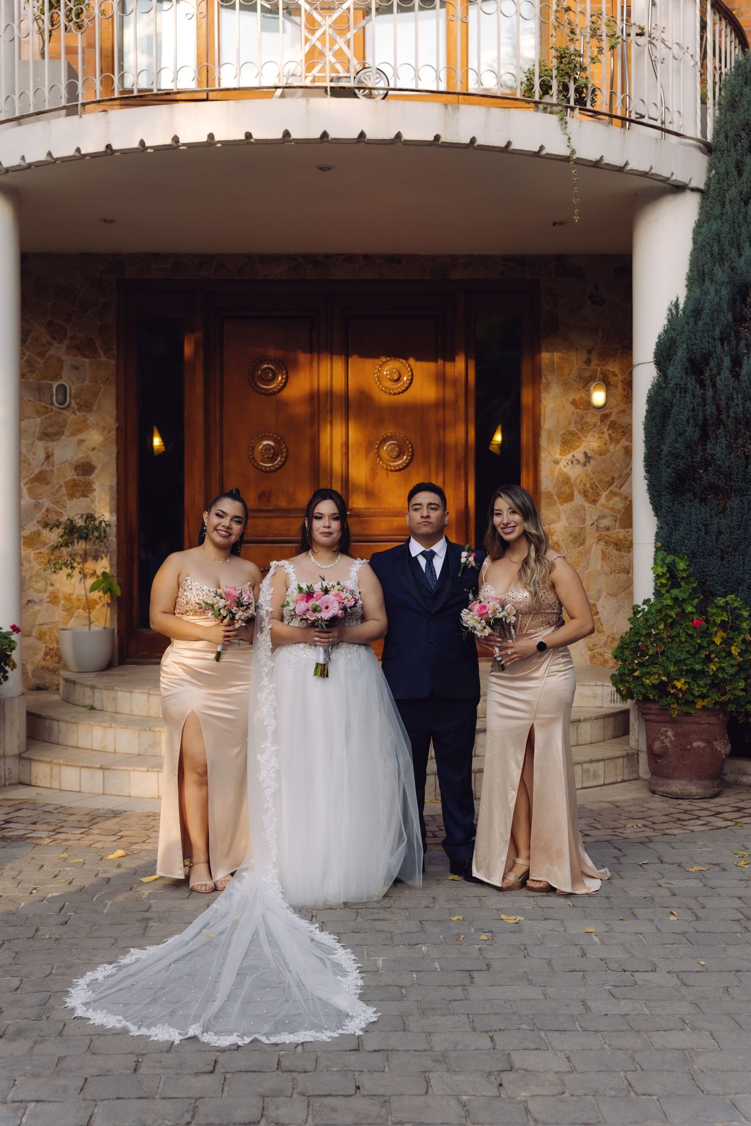 Bride and groom posing with two bridesmaids in champagne dresses outside a stone venue.