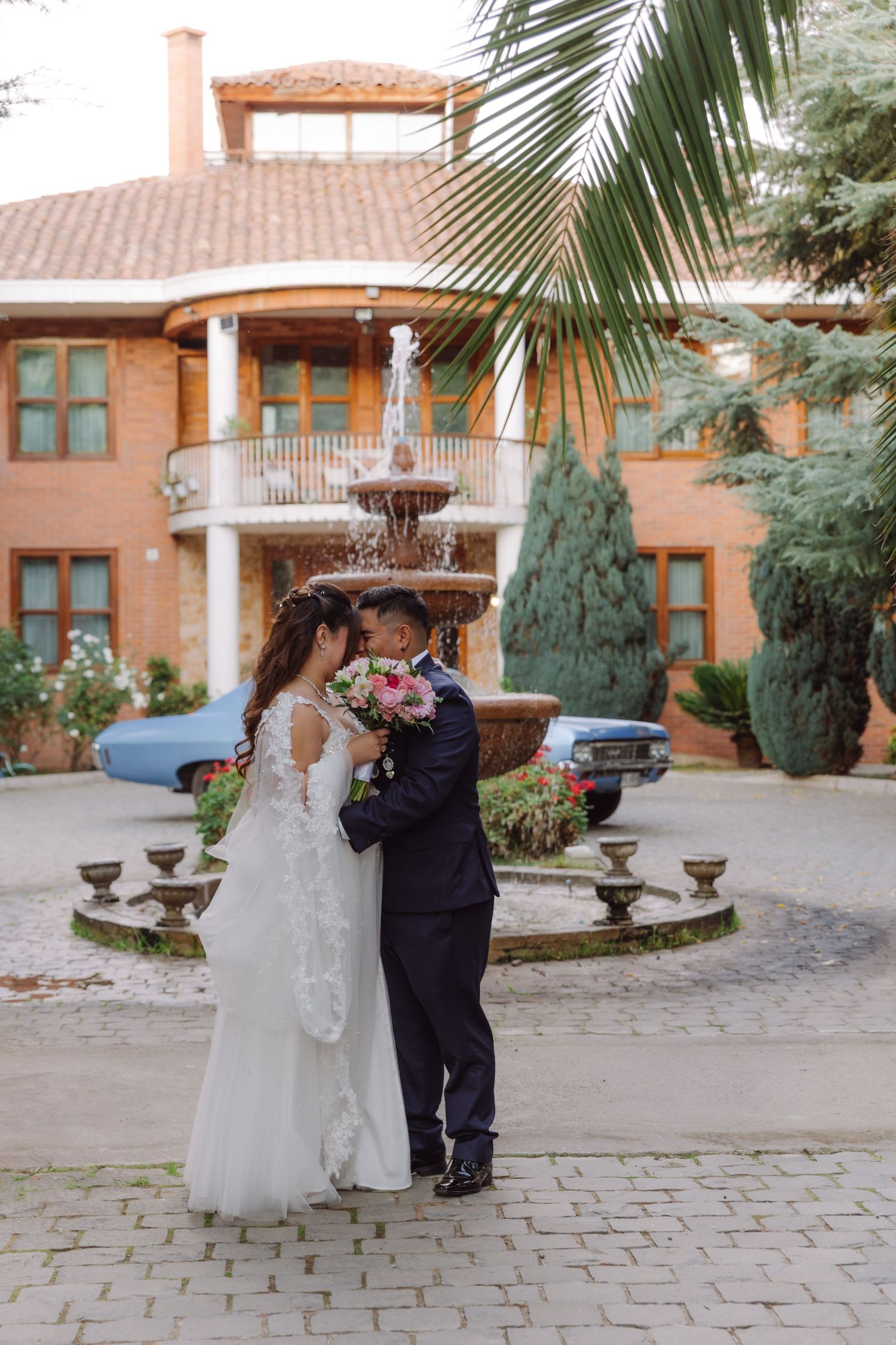 Bride and groom sharing a romantic embrace near a fountain outside a brick venue.