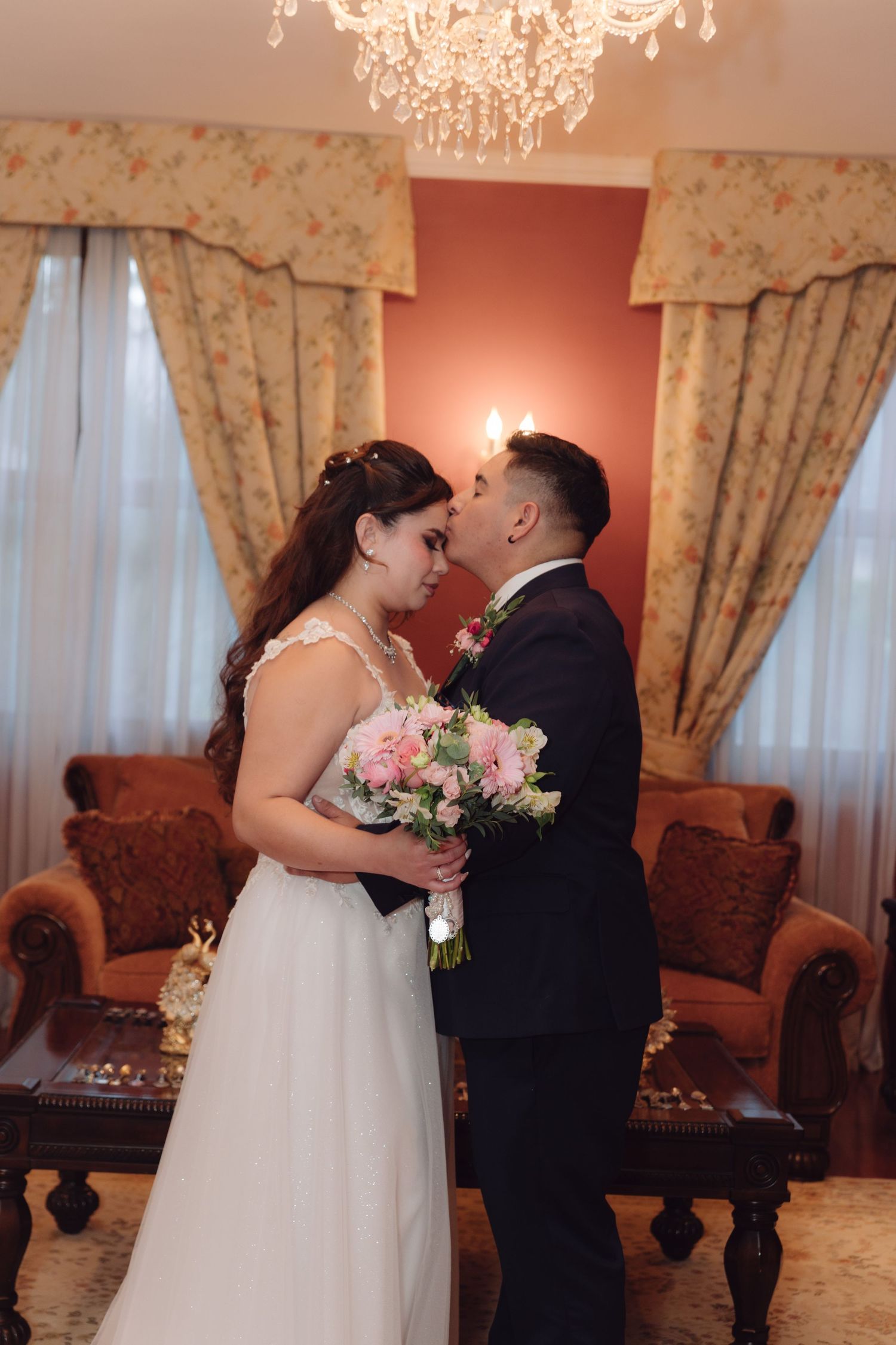 Bride and groom sharing a tender kiss in an elegant chandelier-lit reception room.