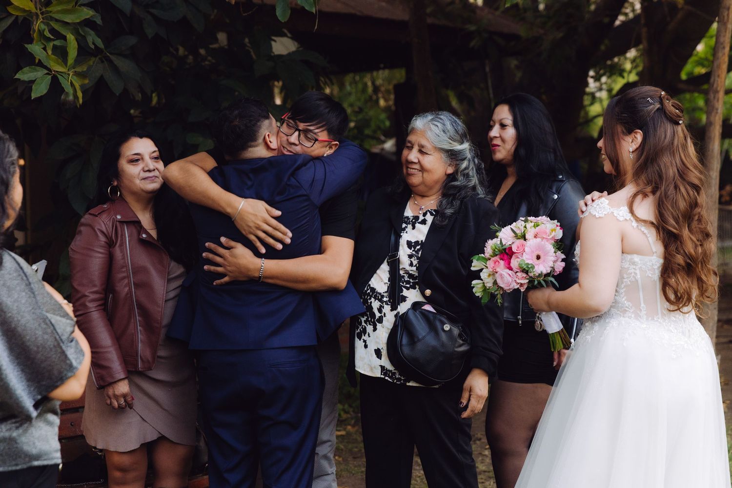 Newlyweds receive warm hugs from family members in an outdoor garden wedding celebration.