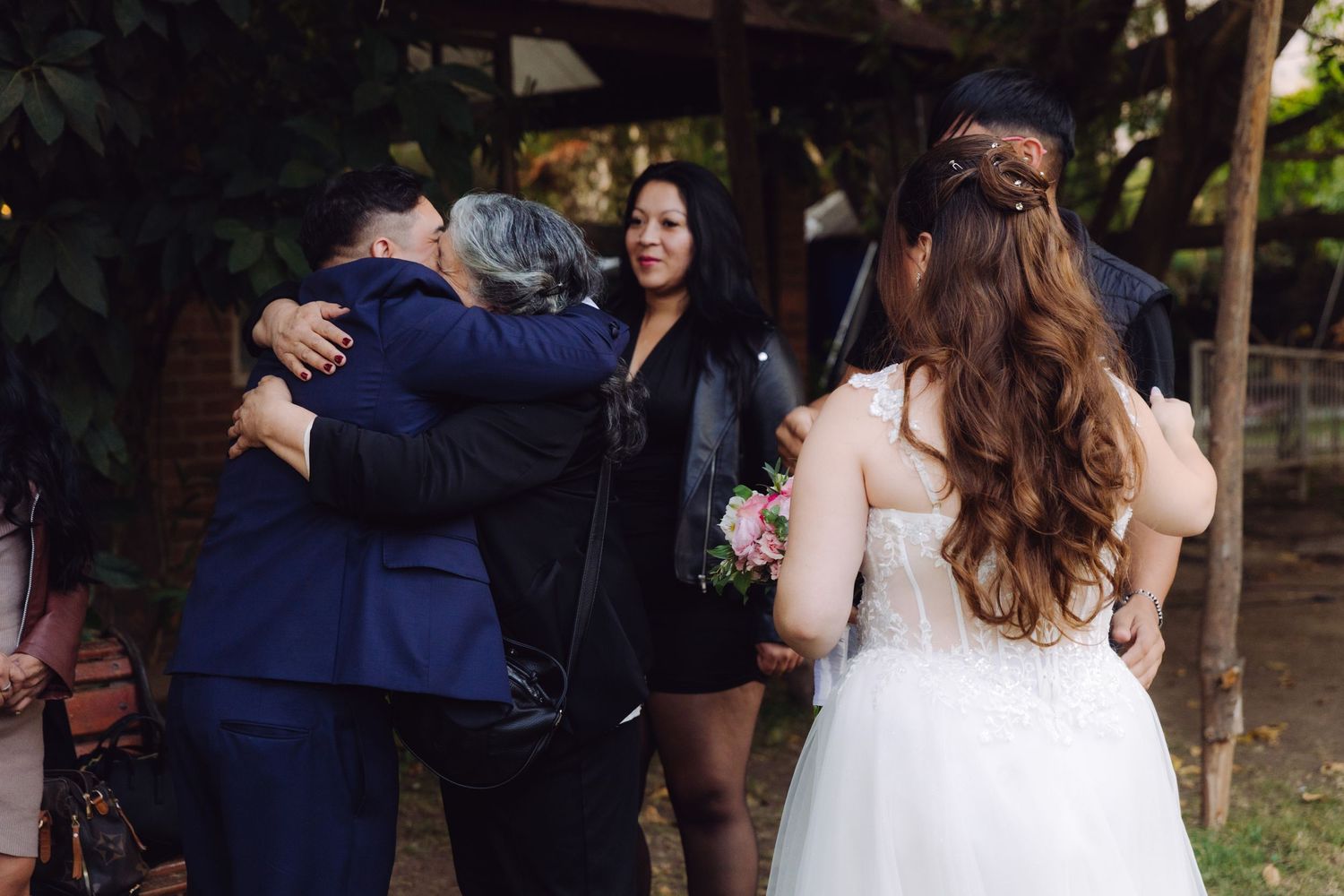 Bride and groom share heartfelt hugs with family guests during outdoor wedding celebrations.