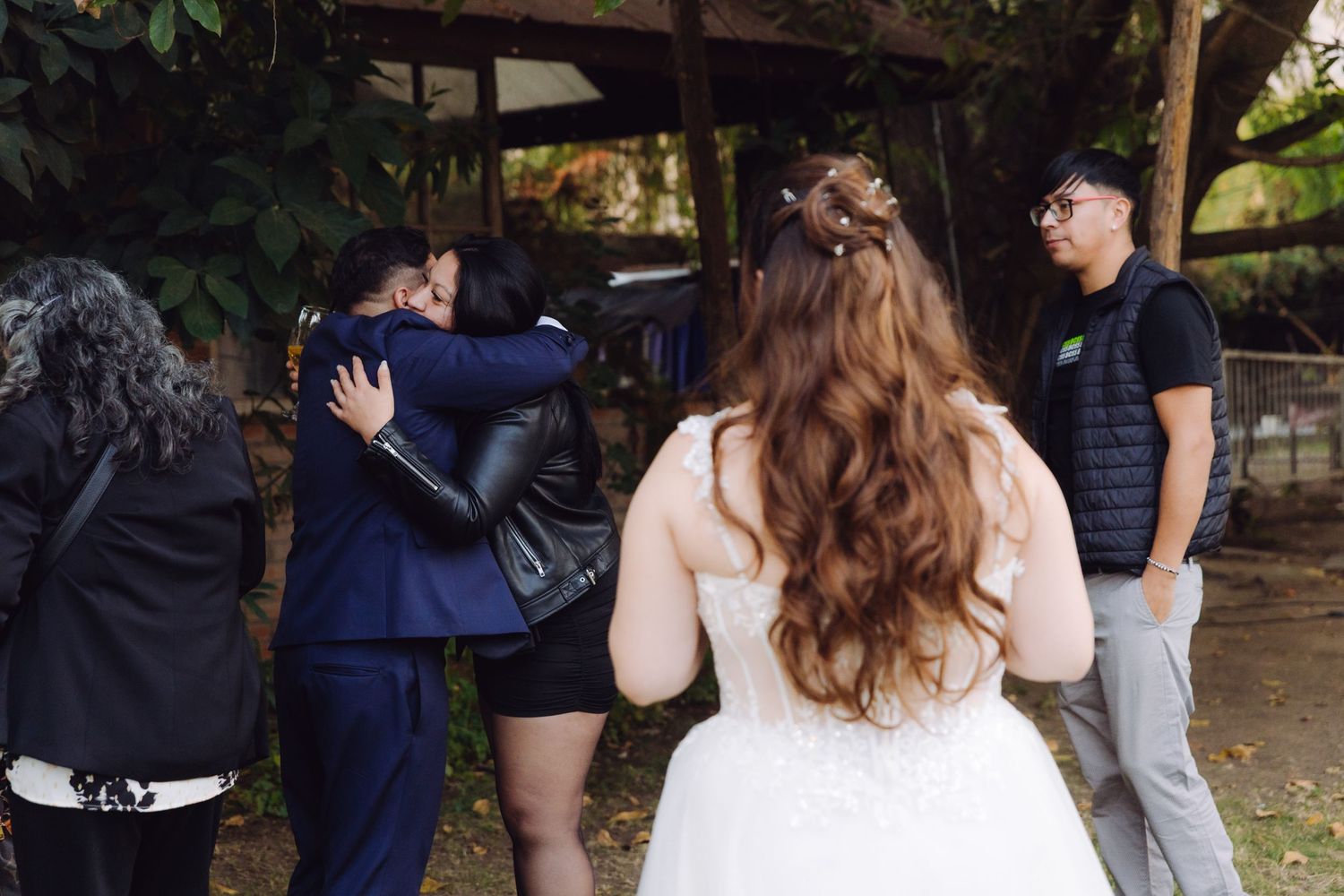 Bride and groom receive congratulatory hugs from guests in a rustic outdoor wedding setting.