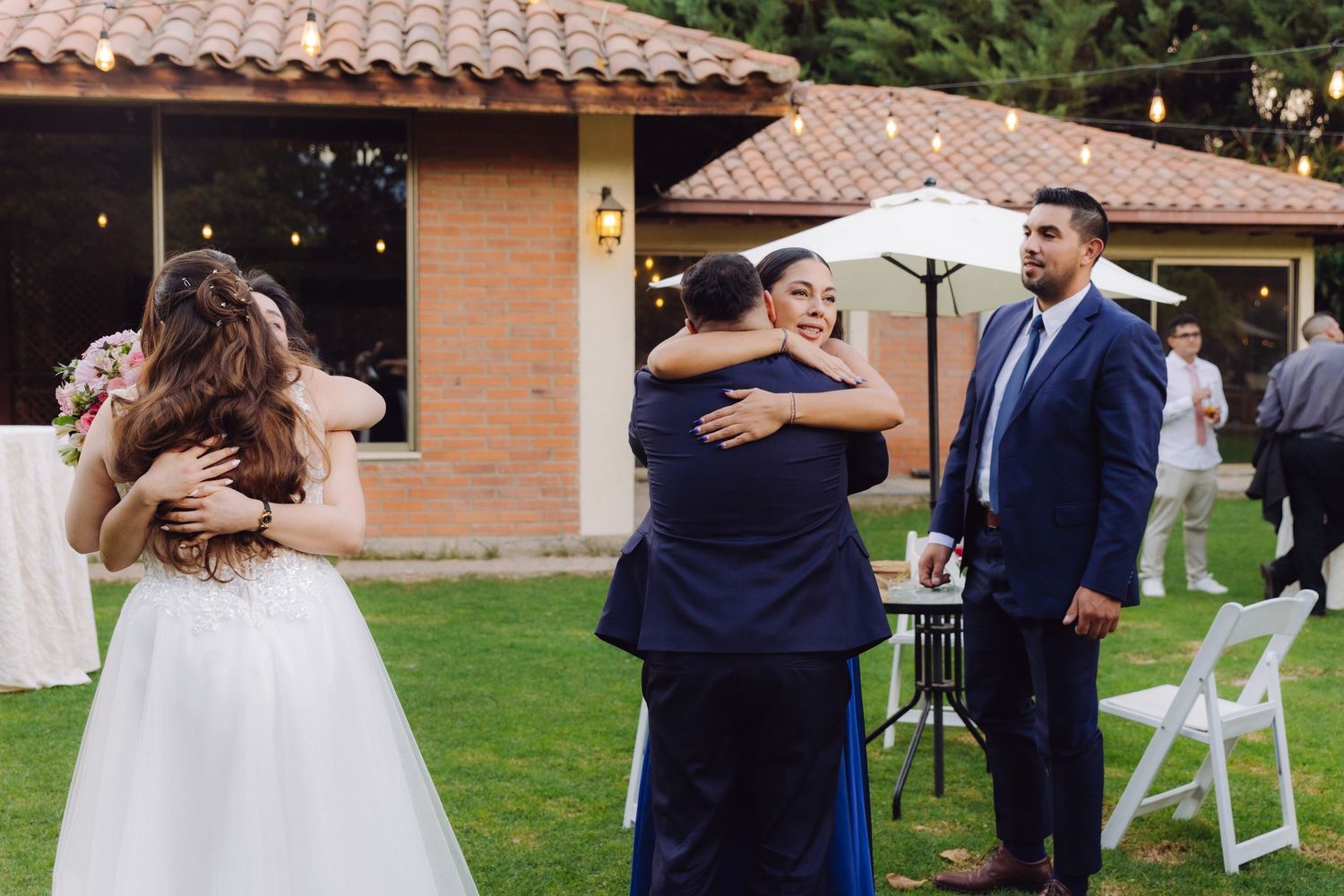 Bride and groom share warm embraces with family guests during an outdoor wedding reception.