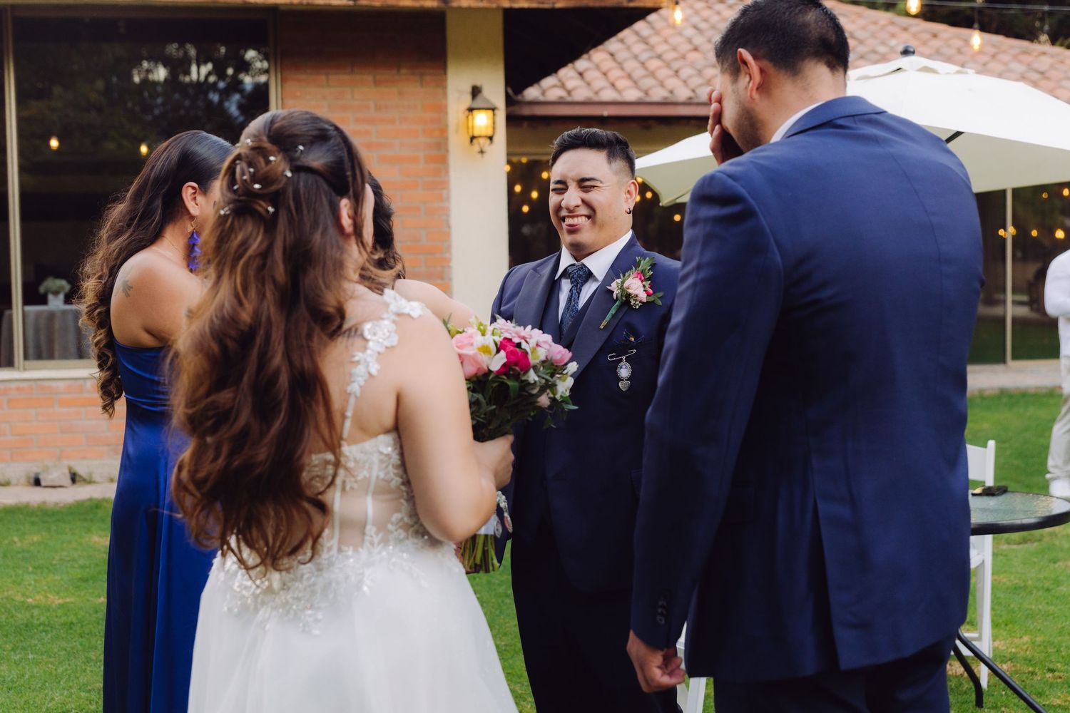 Bride and groom share a joyful moment with wedding party guests during an outdoor ceremony.