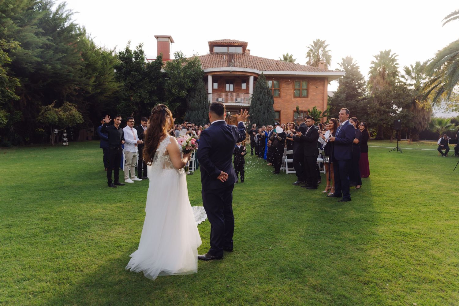 Bride and groom stand together on green lawn during outdoor wedding ceremony at elegant venue.