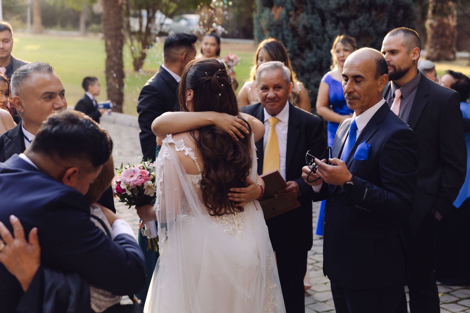 Bride hugs smiling older gentleman while guests celebrate at outdoor wedding reception.