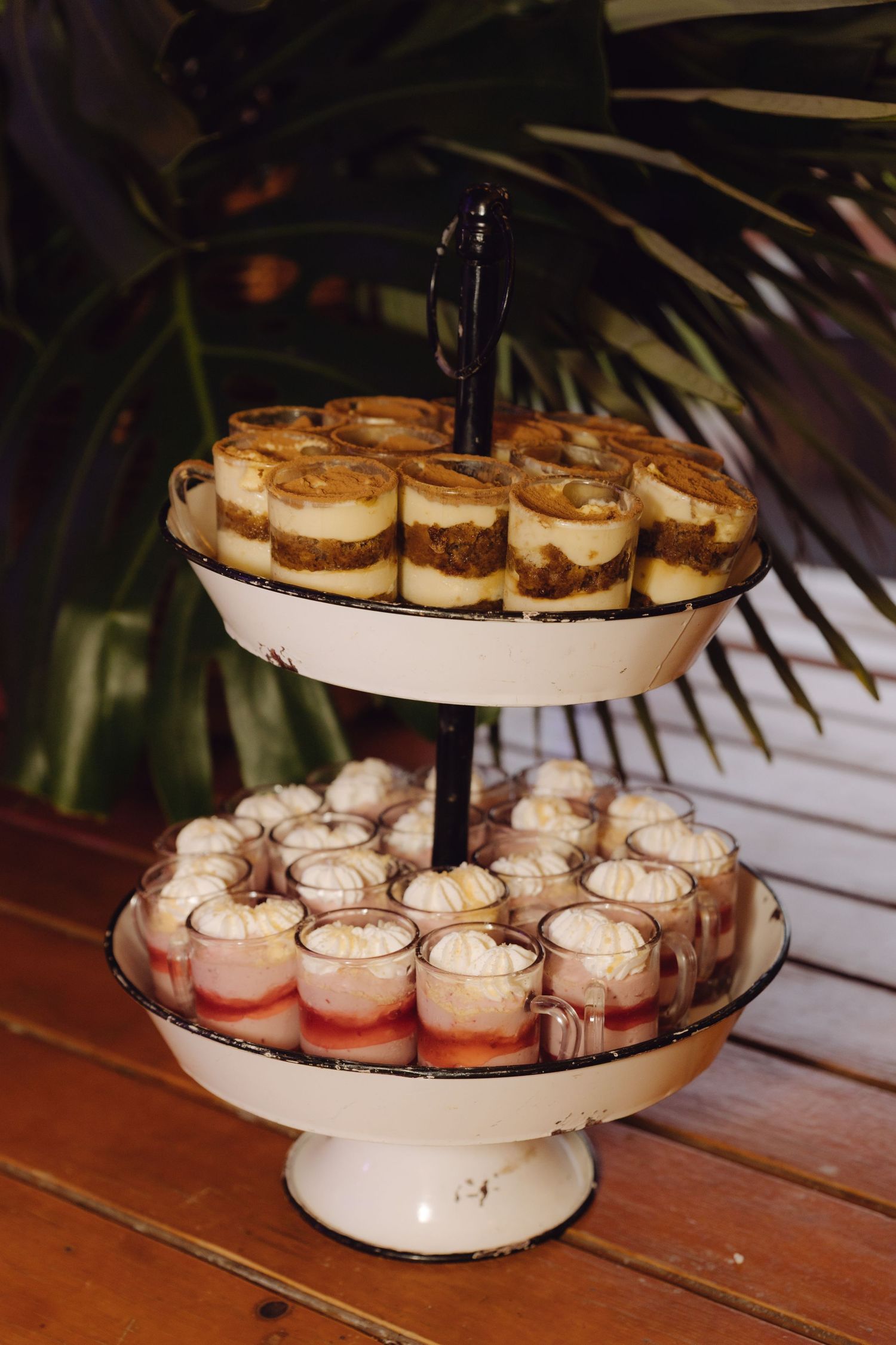 Two-tier vintage white stand displays layered cheesecake cups and pink meringue desserts at wedding reception.
