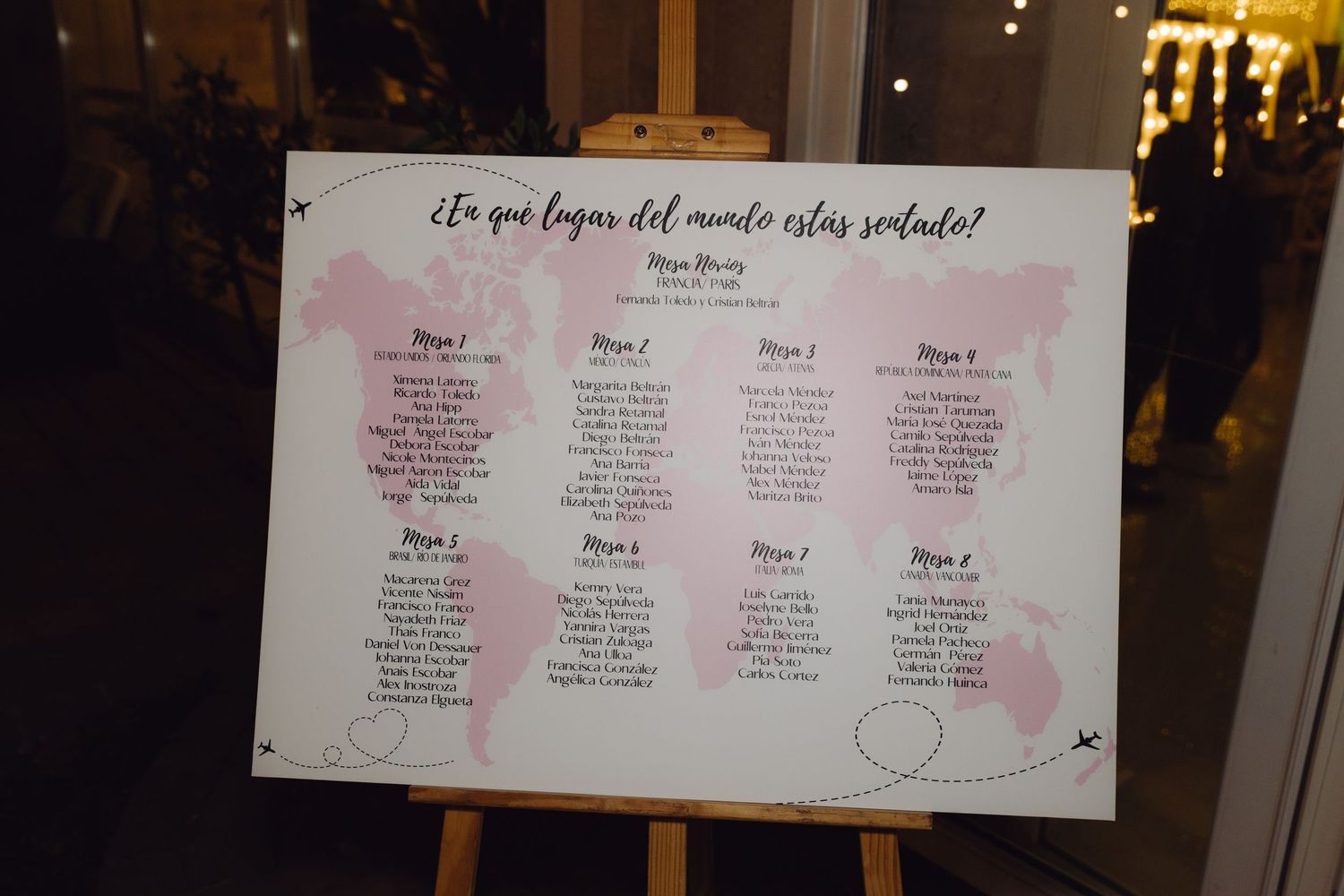 Wedding seating chart on easel with world map design and pink accents titled En que lugar del mundo estas sentado.