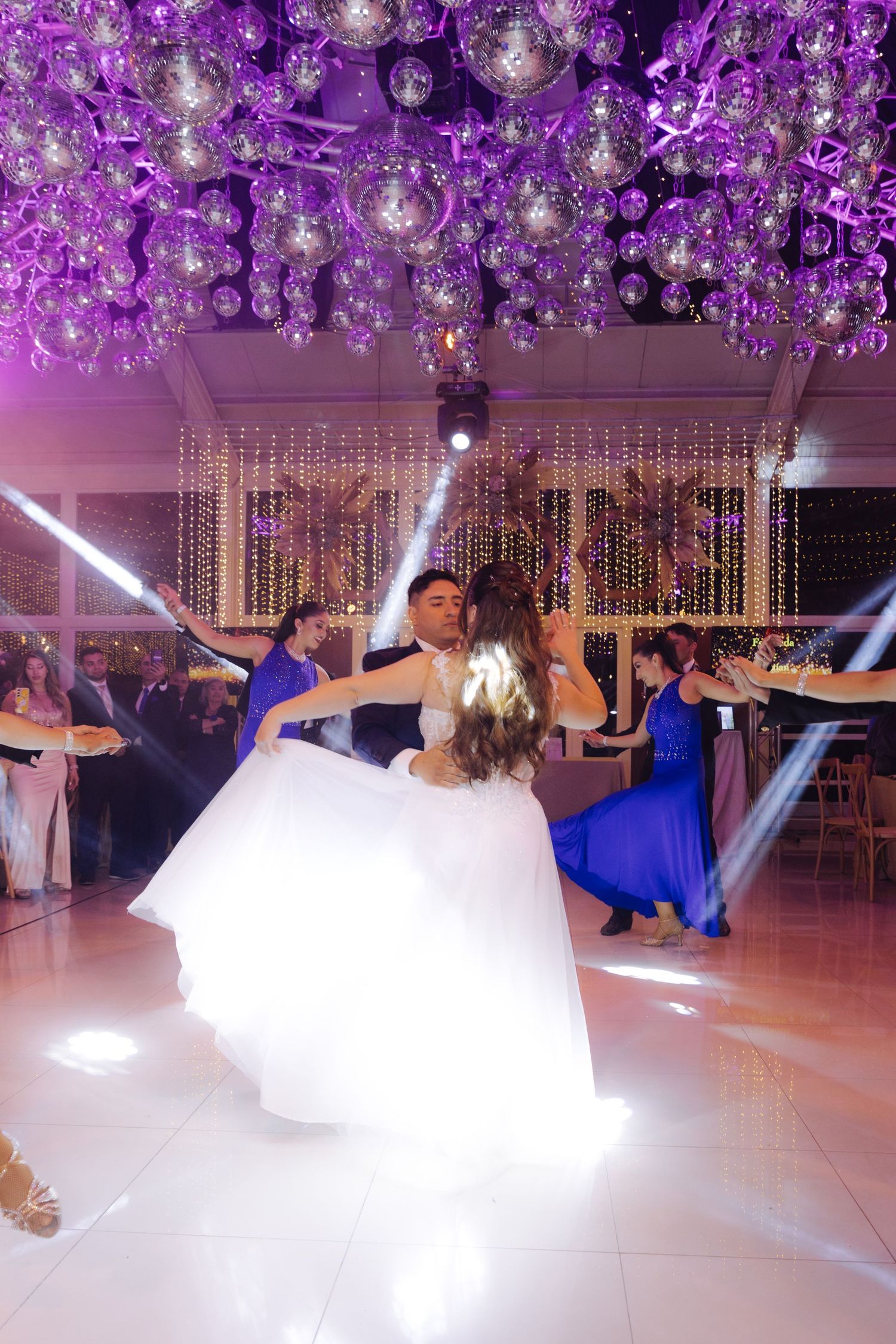 Bride twirls in white gown during first dance with groom under disco ball ceiling at wedding.