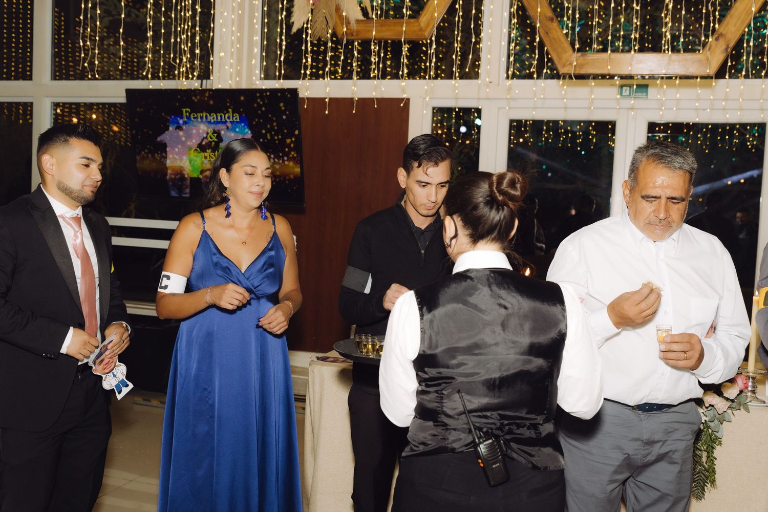 Wedding guests in formal attire socializing on dance floor with fairy lights and decorations in background.