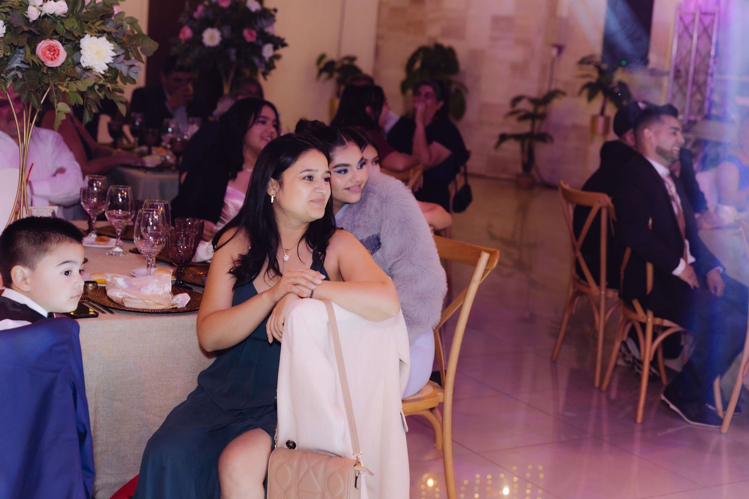 Couple sharing an intimate moment seated at wedding reception table with other guests in background.