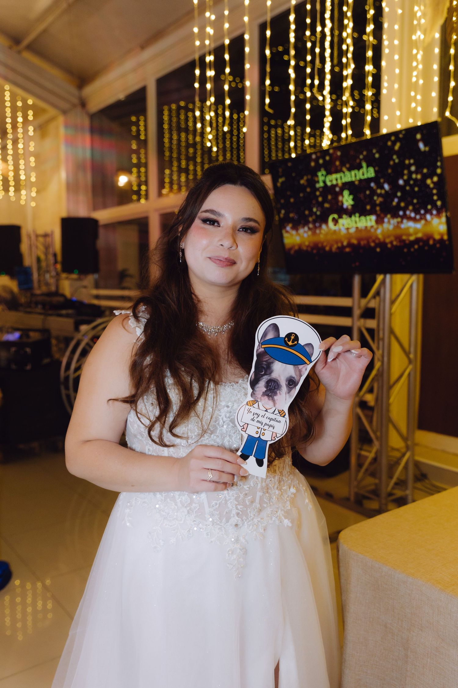 Beautiful bride in white gown holding a fun dog photo booth prop at her wedding reception.