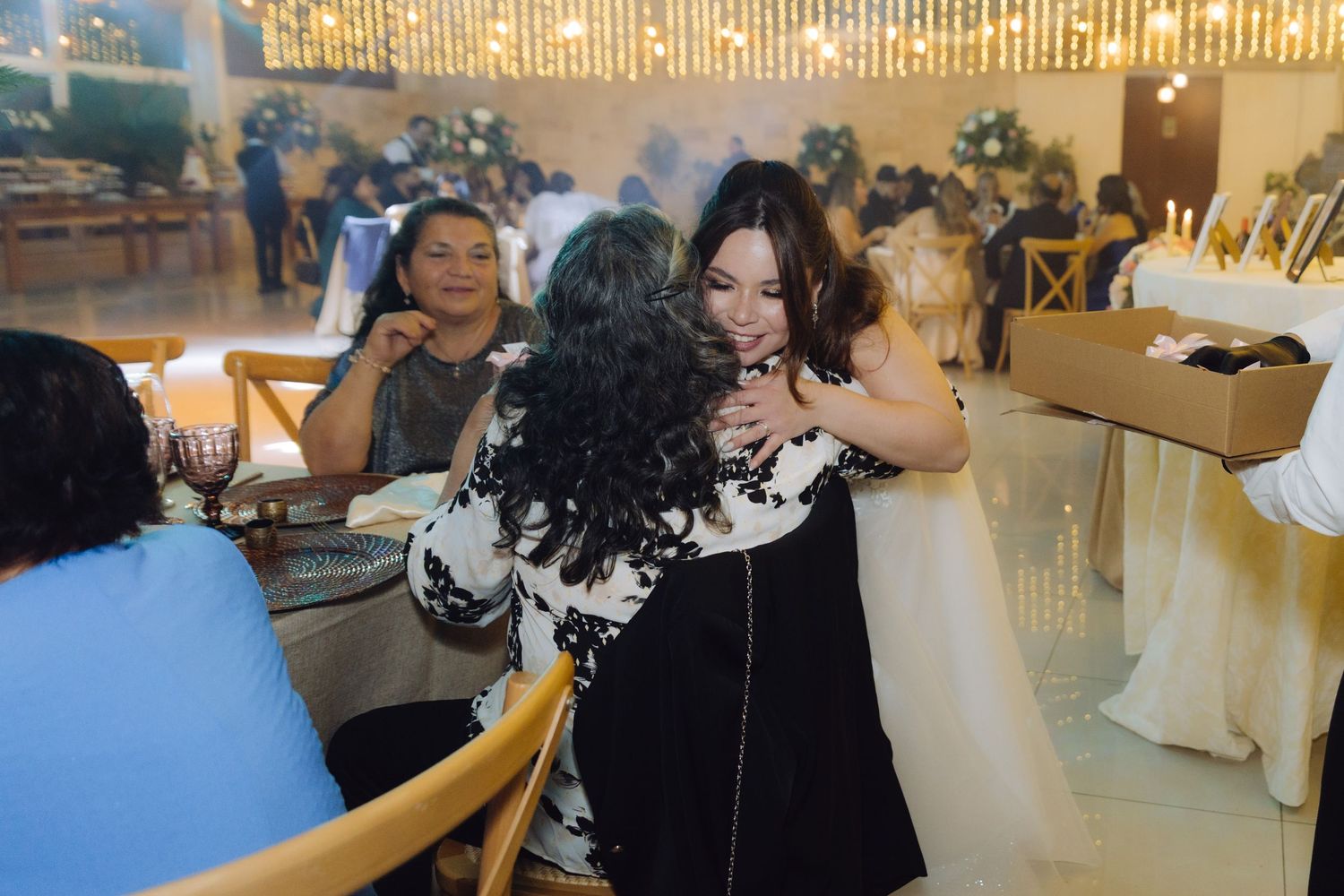 Bride in white wedding gown sharing a warm embrace with a guest at the reception.