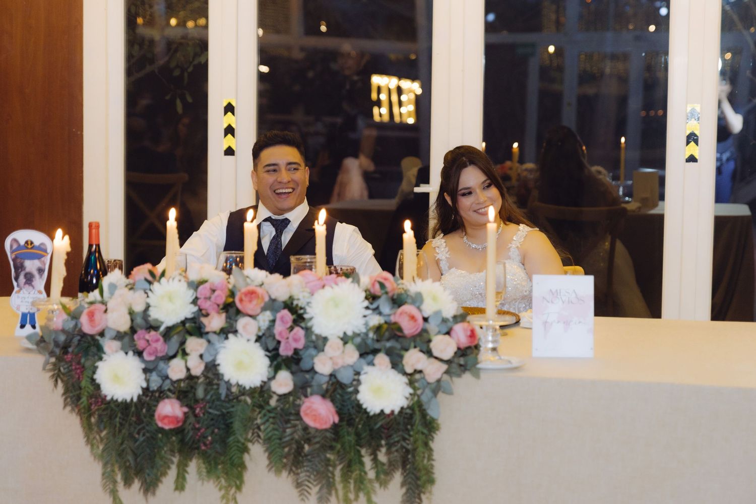 Bride and groom smiling together at the sweetheart table adorned with pink and white flowers.