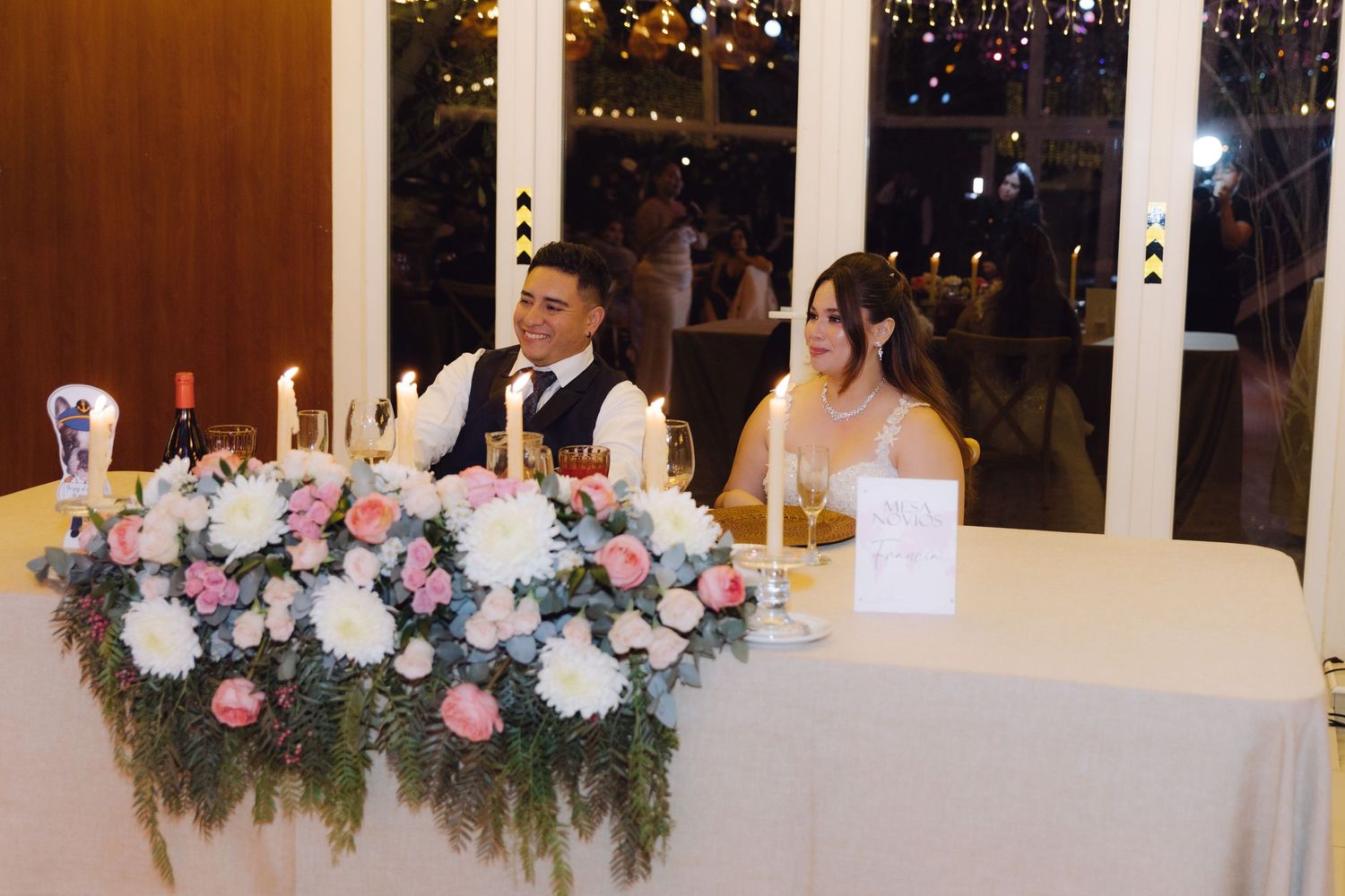 Bride and groom seated at sweetheart table adorned with pink and white floral centerpiece at wedding reception.