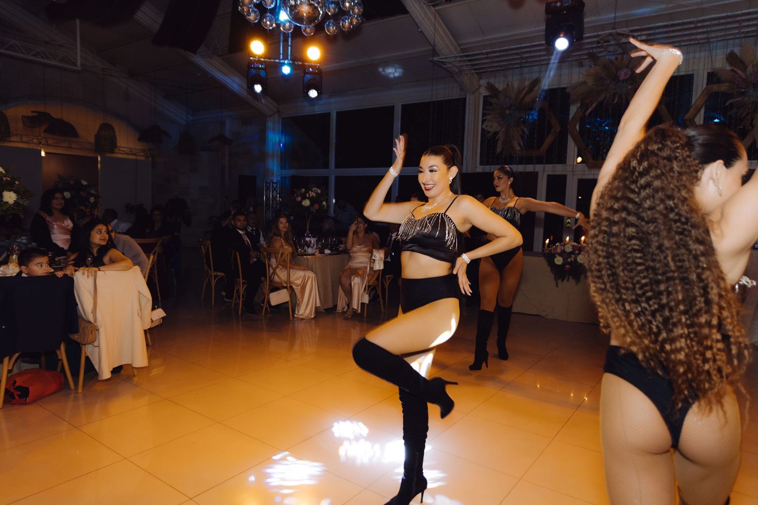 Energetic dance performers in black costumes entertaining guests on lit dance floor at wedding reception.