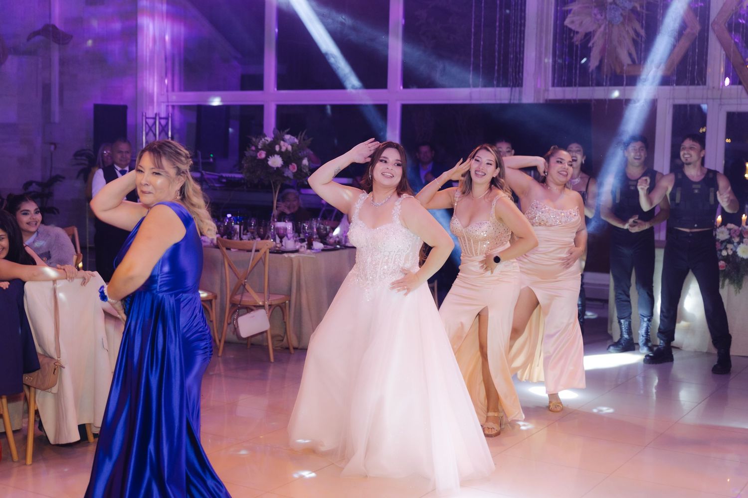 Bride in white ball gown dancing with bridesmaids in blue and gold dresses at wedding reception.
