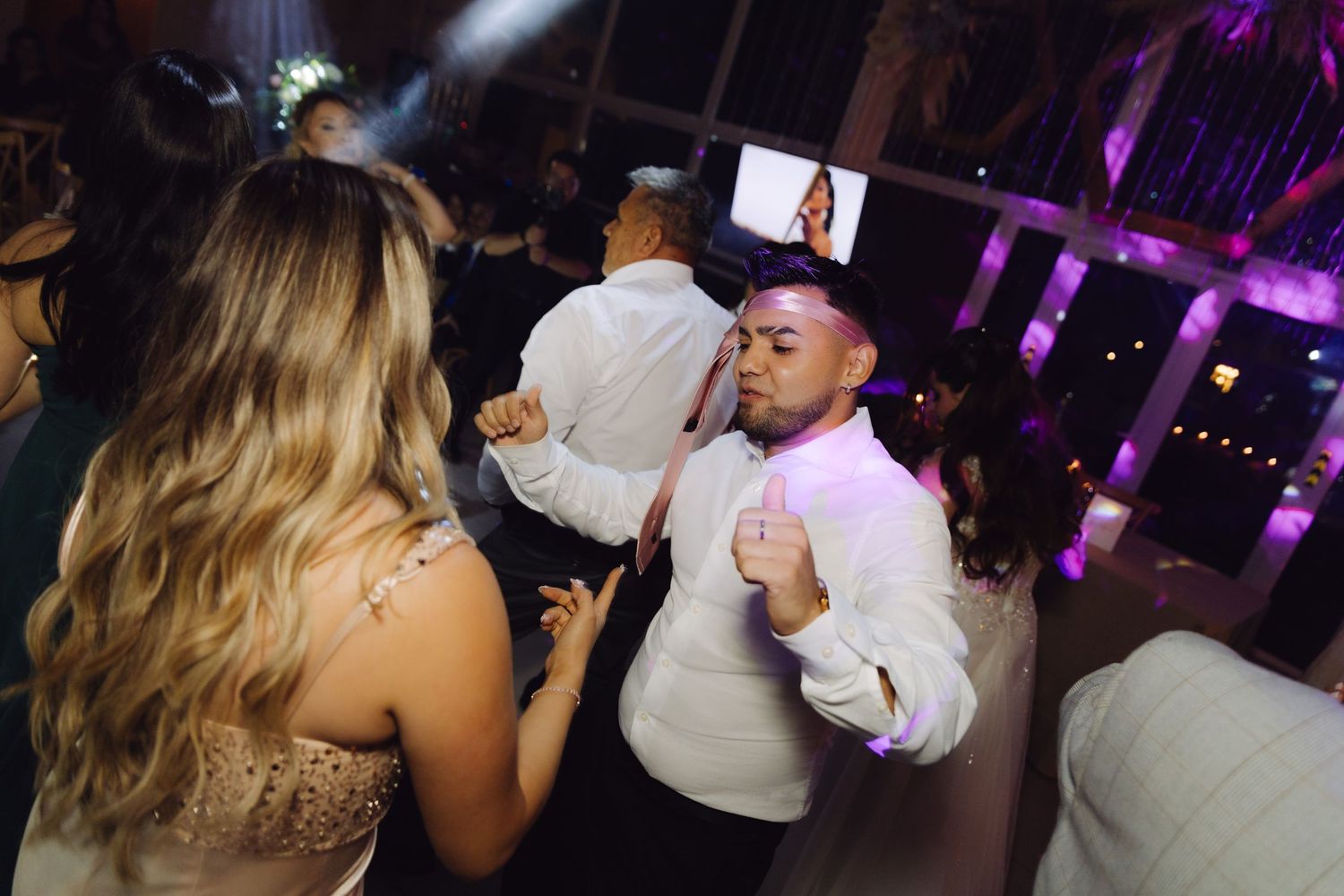 Wedding guests dancing closely together on crowded dance floor during lively evening reception celebration.