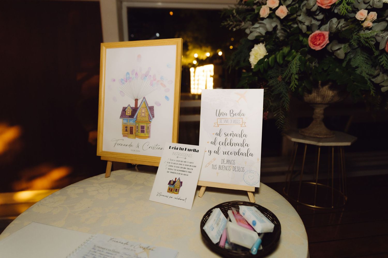 Elegant wedding welcome table with Up-themed artwork, guest book, and floral arrangement at evening reception.