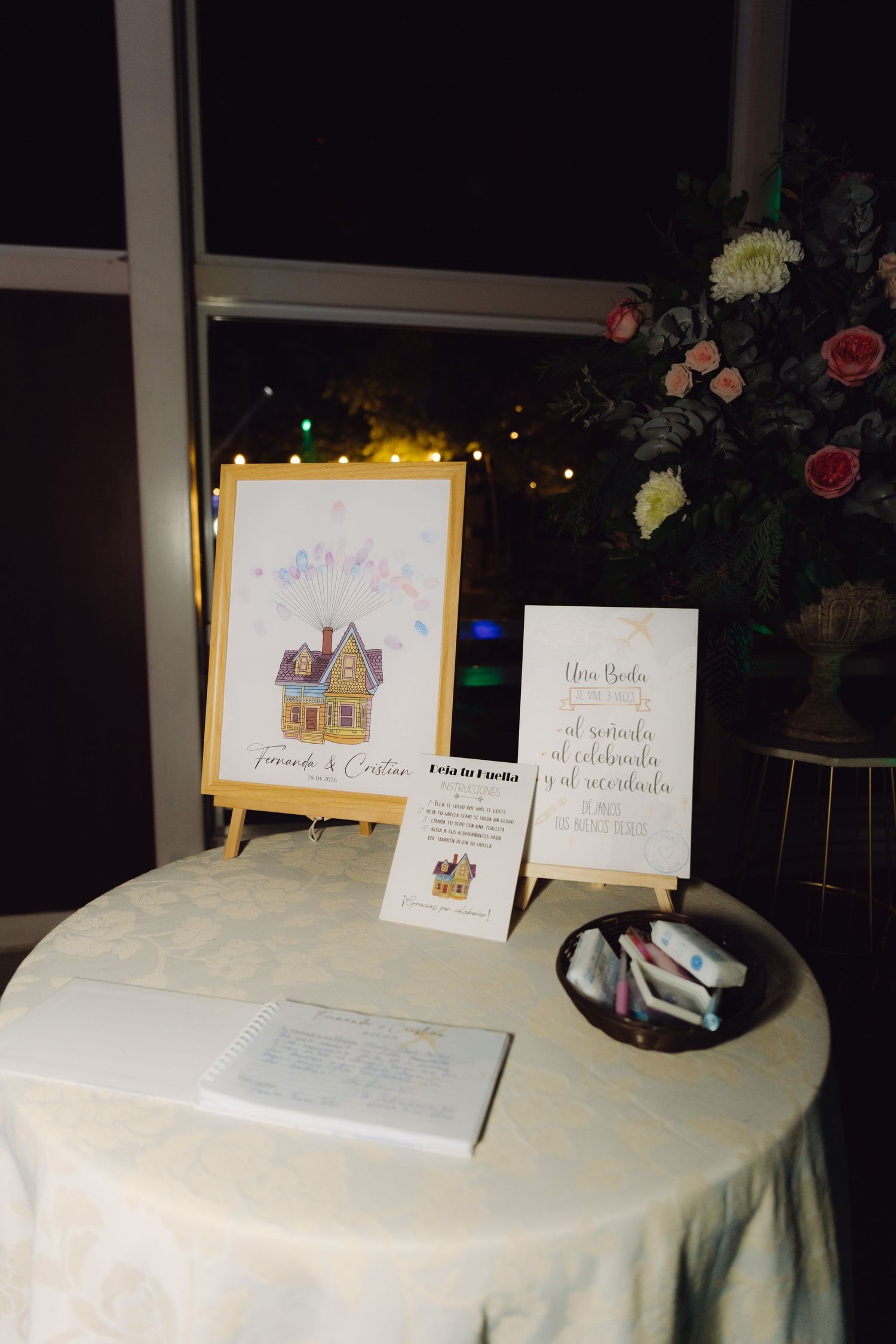 Wedding guest book table featuring Up movie house illustration, sign, and pink floral centerpiece at night.