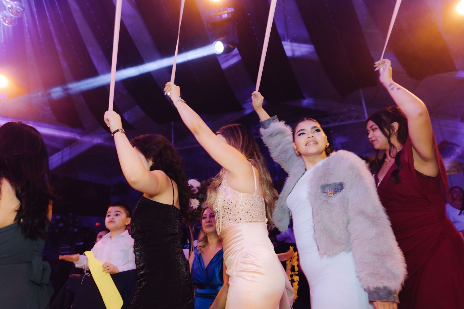 Excited wedding guests pulling ribbon wands under purple lights on the dance floor at reception.