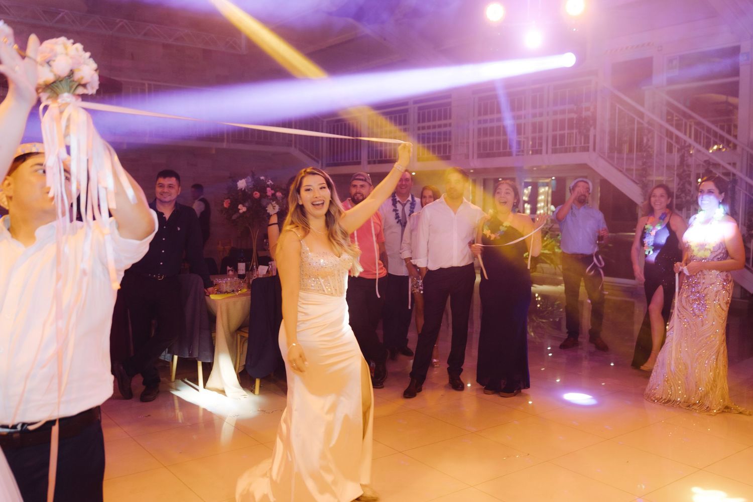 Bride in gold gown tossing bouquet with ribbon streamers to guests on wedding dance floor.