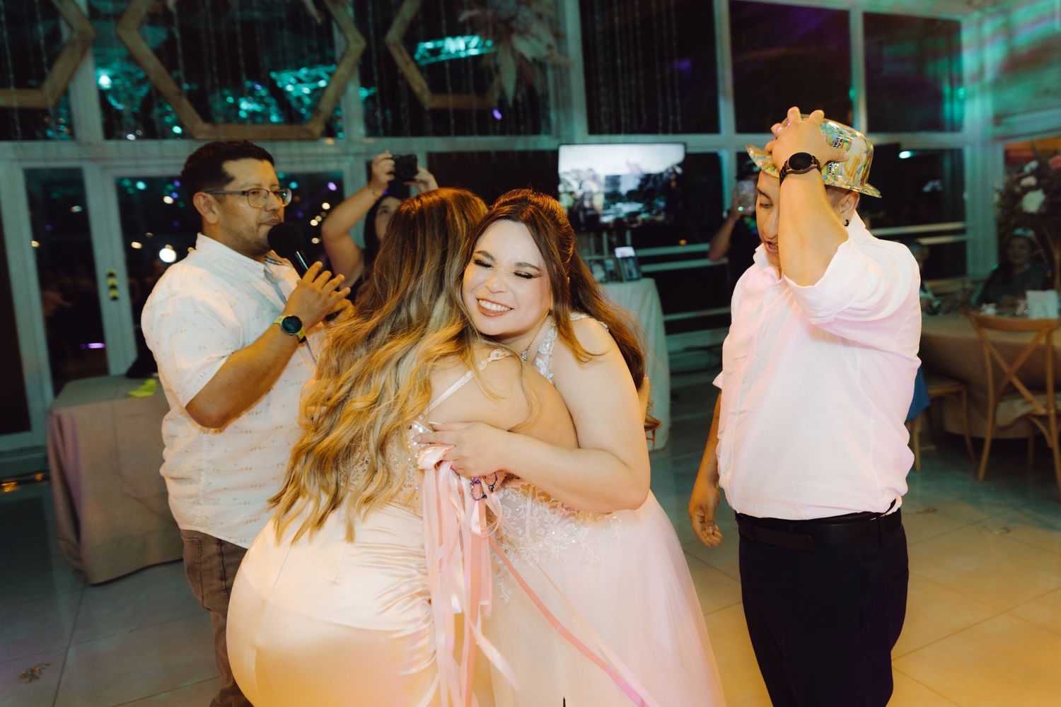 Wedding guests dancing and embracing on dance floor during evening reception celebration.