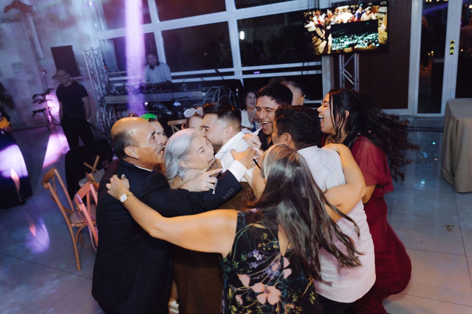 Joyful wedding guests sharing a group hug on the dance floor during a lively reception party.
