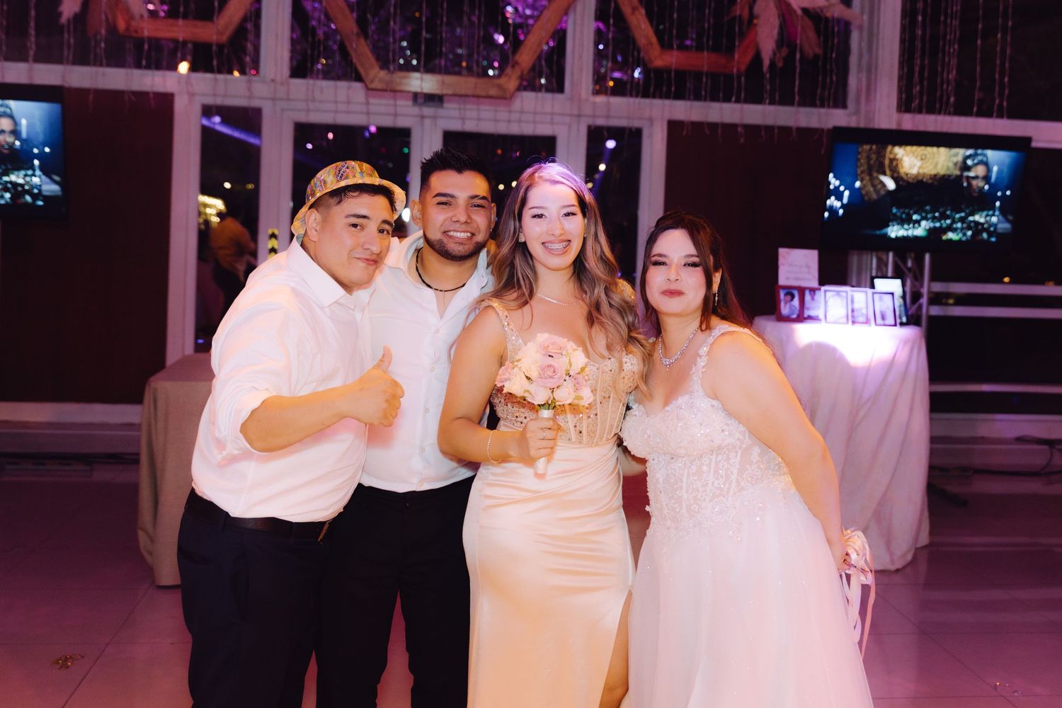 Bride holding bouquet poses with three guests at a wedding reception in a decorated venue.