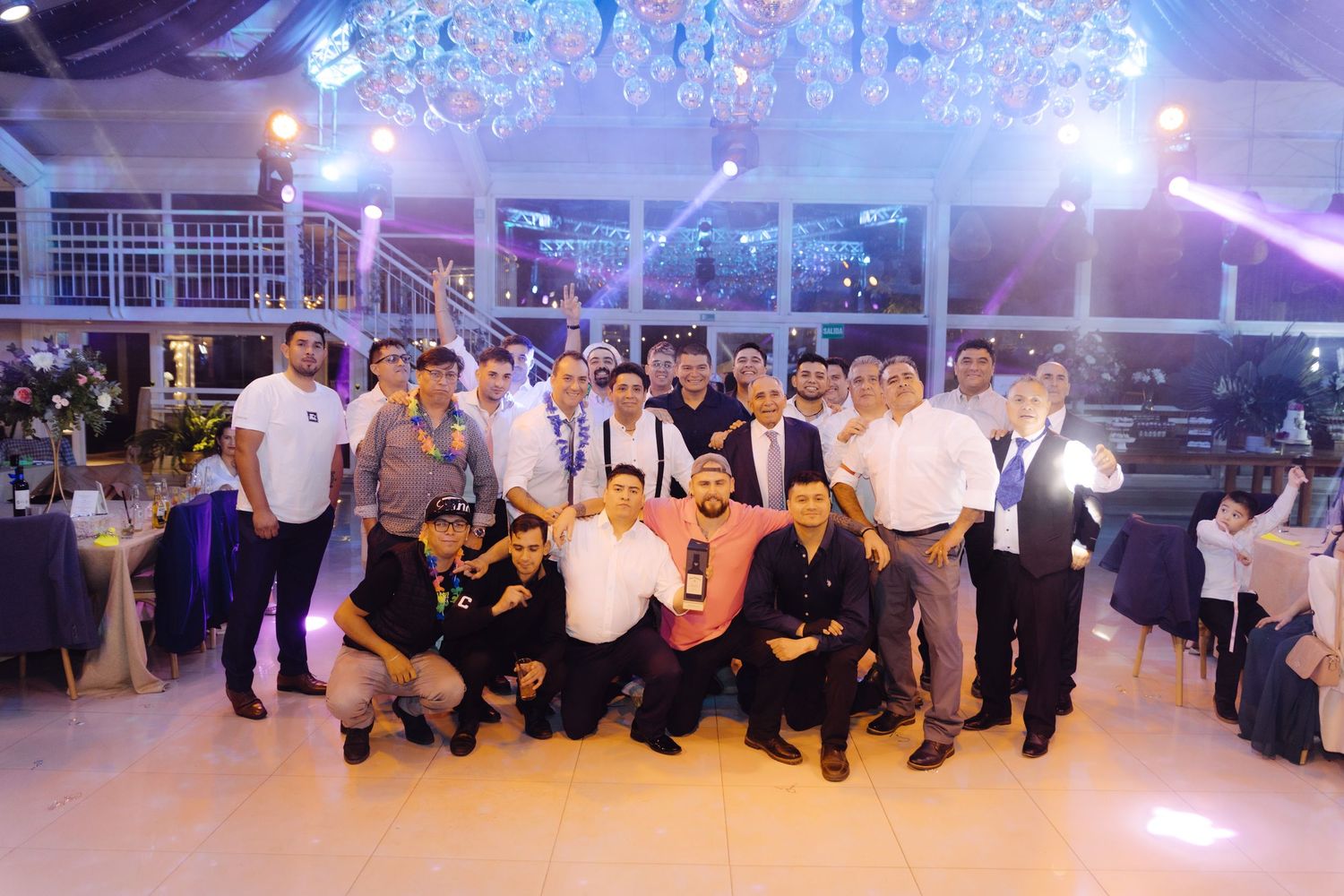 Large group of wedding guests posing together for a photo in a beautifully lit reception hall.
