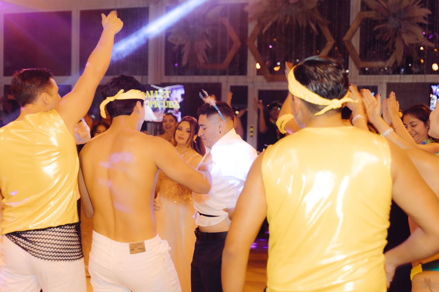 Guests dancing energetically at a lively wedding reception party with yellow themed outfits under bright lights.