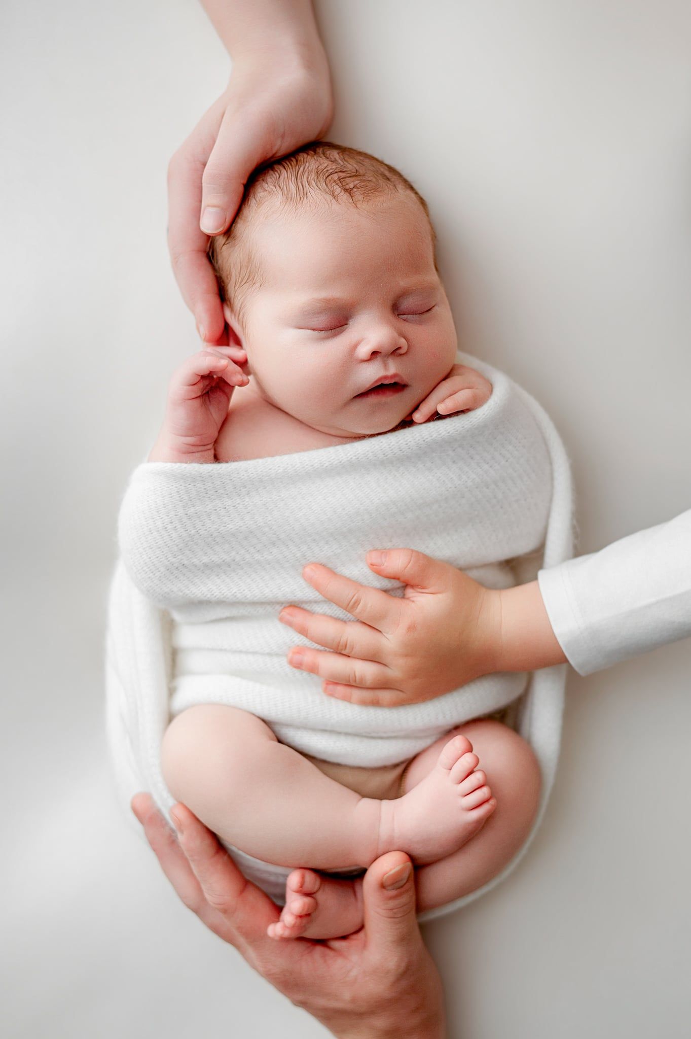 Relaxed studio newborn photography collage featuring a sleeping baby wrapped in white fabric with delicate accessories.