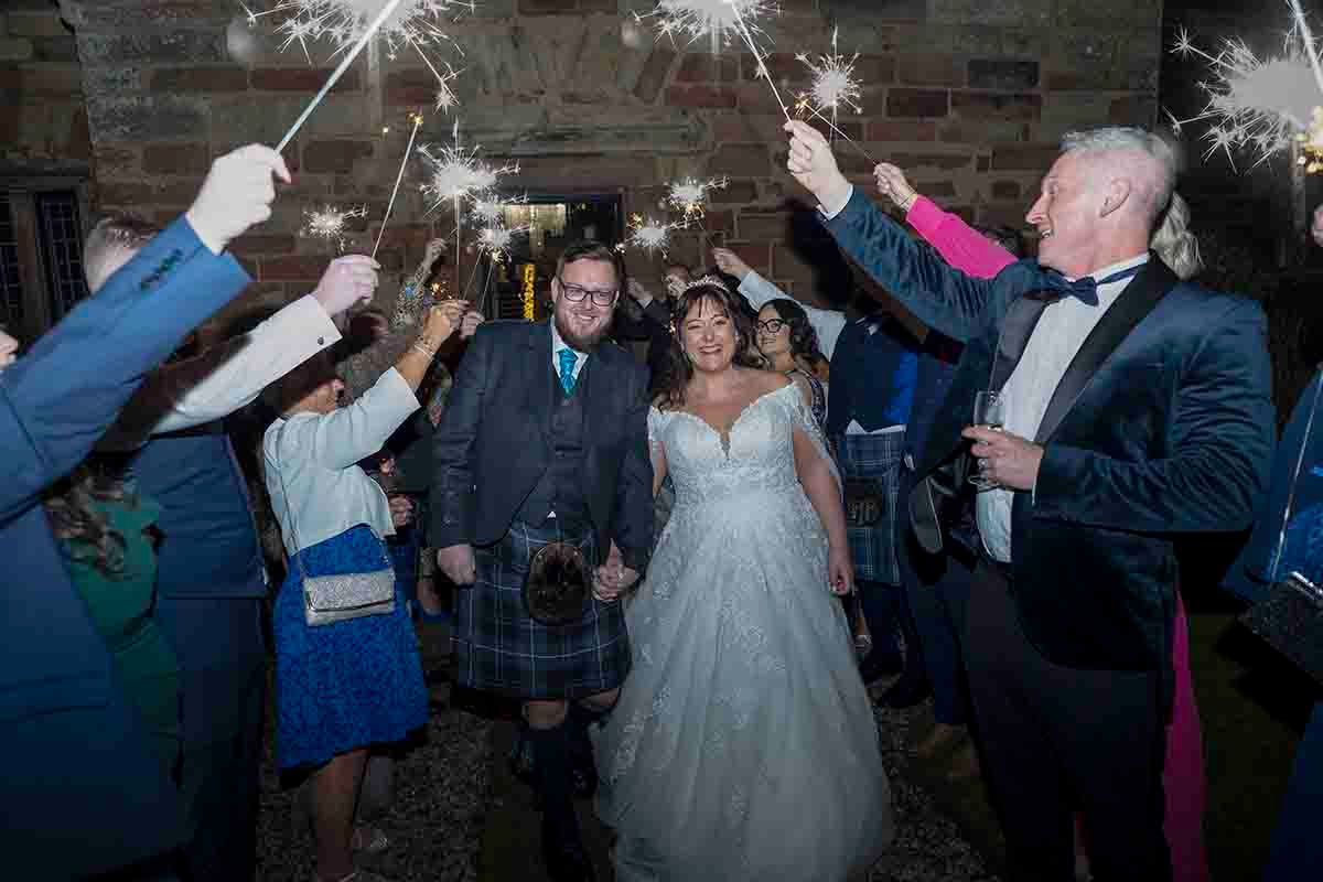 Bride and groom leave the baronial hall at Dalston Hall to a sparkler reception instead of confetti