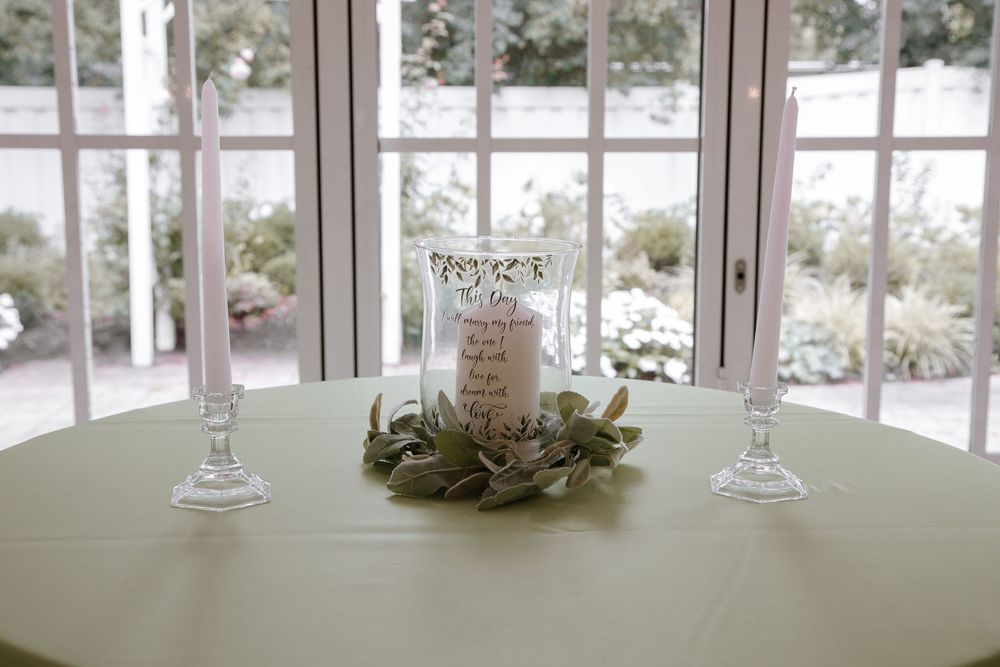 Elegant wedding memorial candle centerpiece with greenery wreath and taper candles on sage green tablecloth.