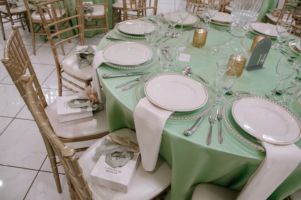 Elegant wedding reception table with mint green tablecloth, white plates, gold chairs, and crystal glassware.