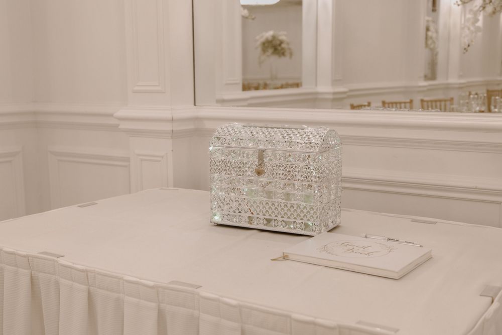 Elegant white jeweled box on a draped table with a mirror and ornate white paneling in a luxurious room.